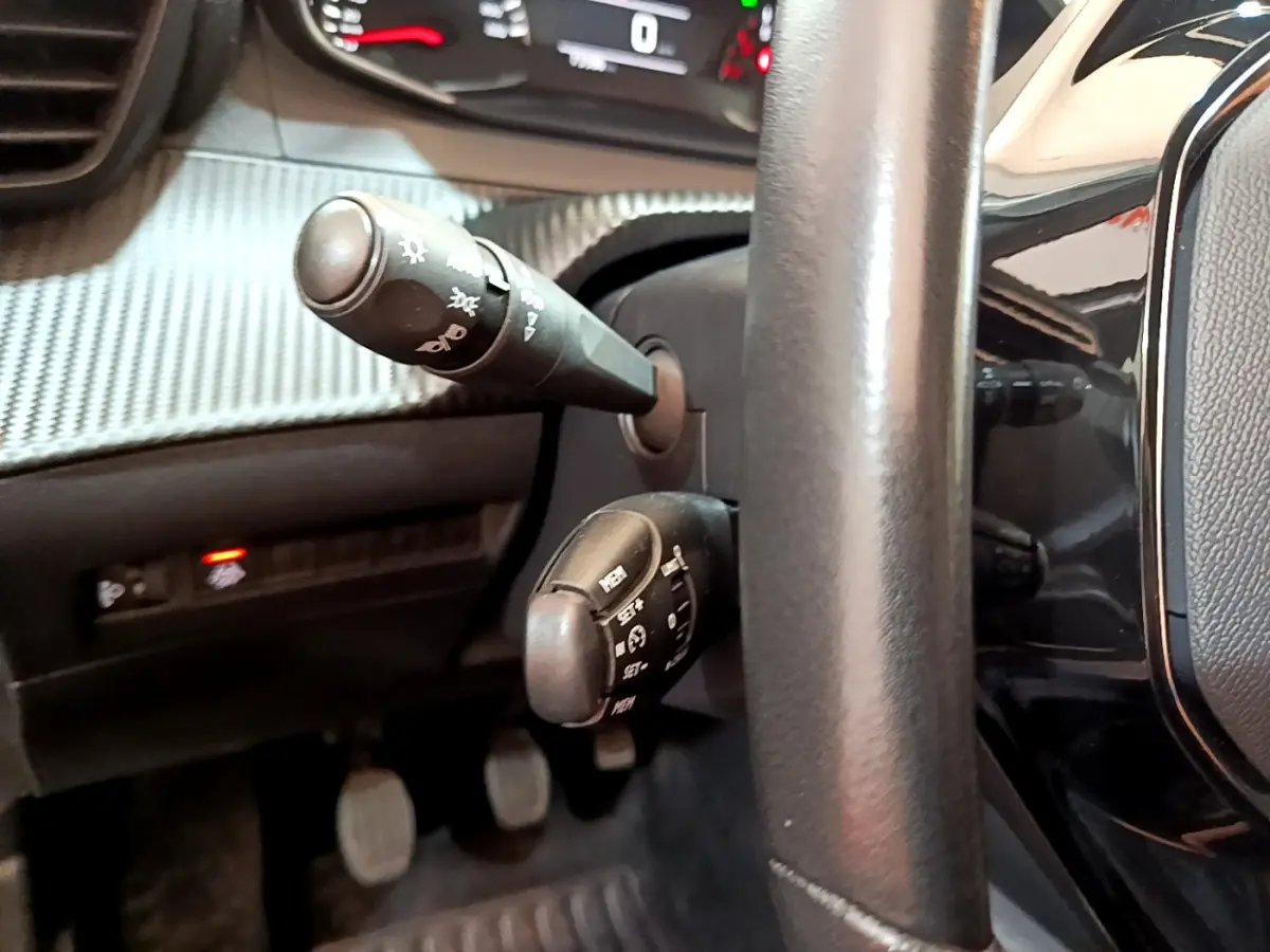 Gros plan sur les commandes au volant cuir noir d'une Peugeot 2008 2020, avec tableau de bord et pédales visibles.