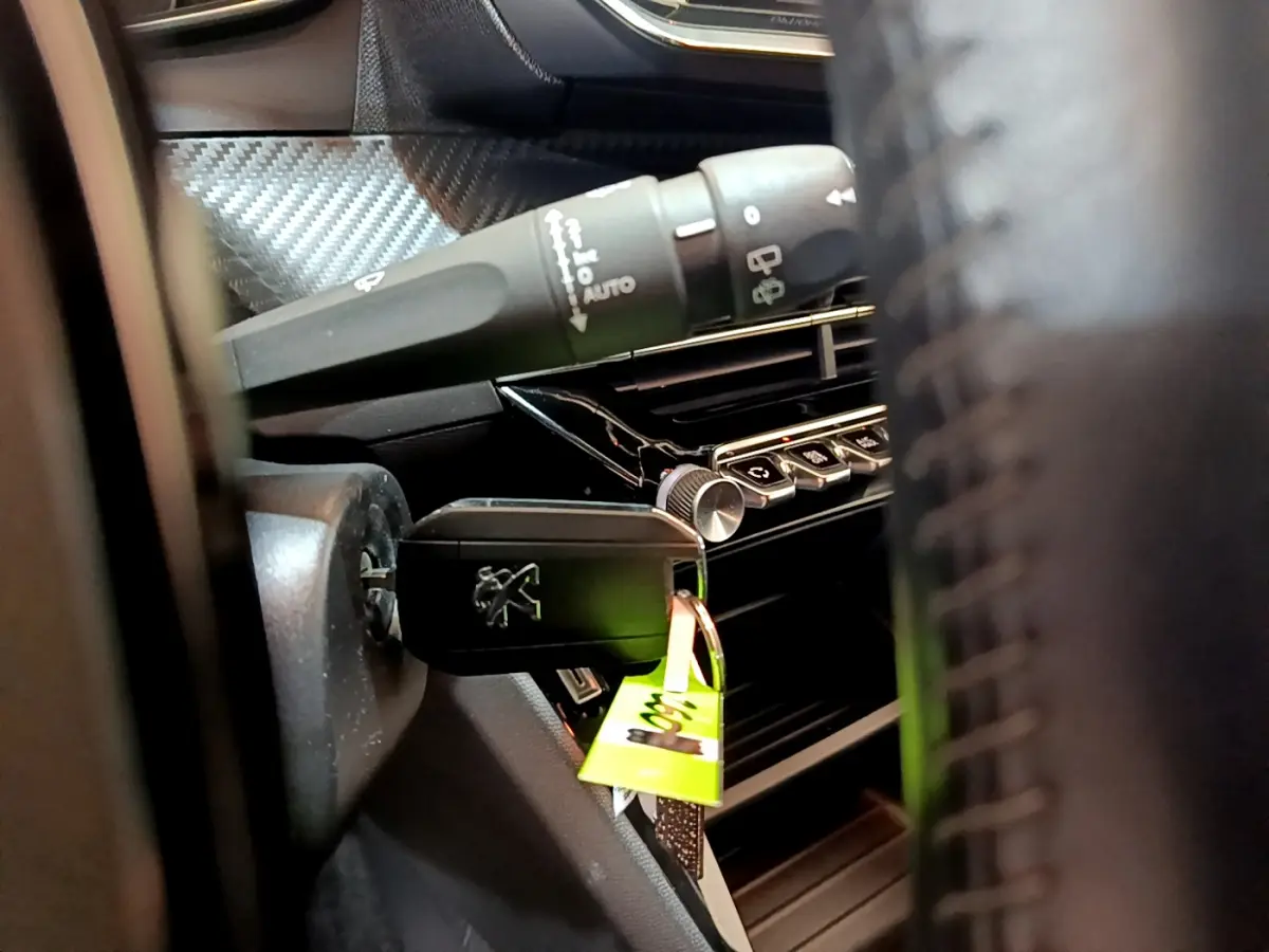 Gros plan sur la clé insérée dans le contacteur d'une Peugeot 2008 gris clair, avec commandes du tableau de bord visibles.