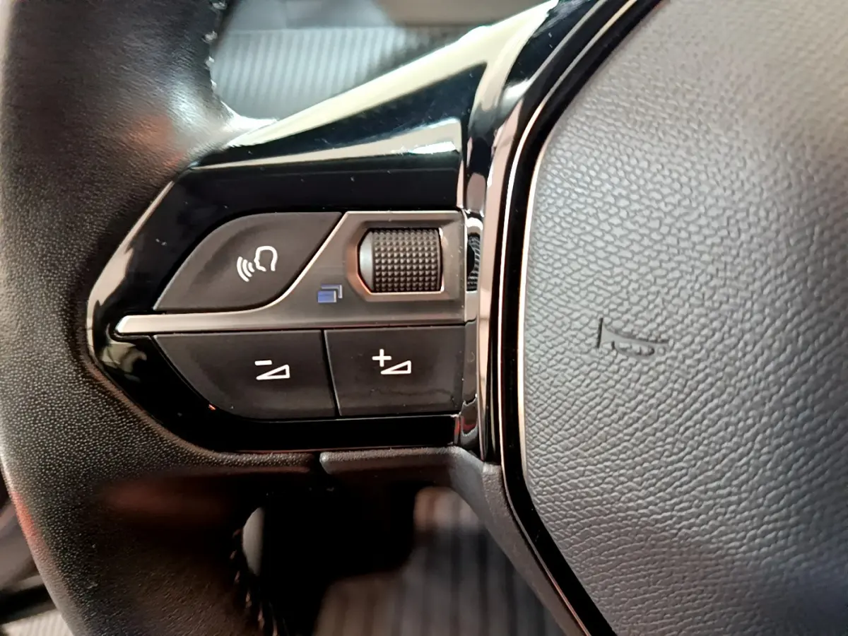 Gros plan sur les commandes gauche du volant cuir noir du Peugeot 2008 gris clair, version 2020 Active Business.