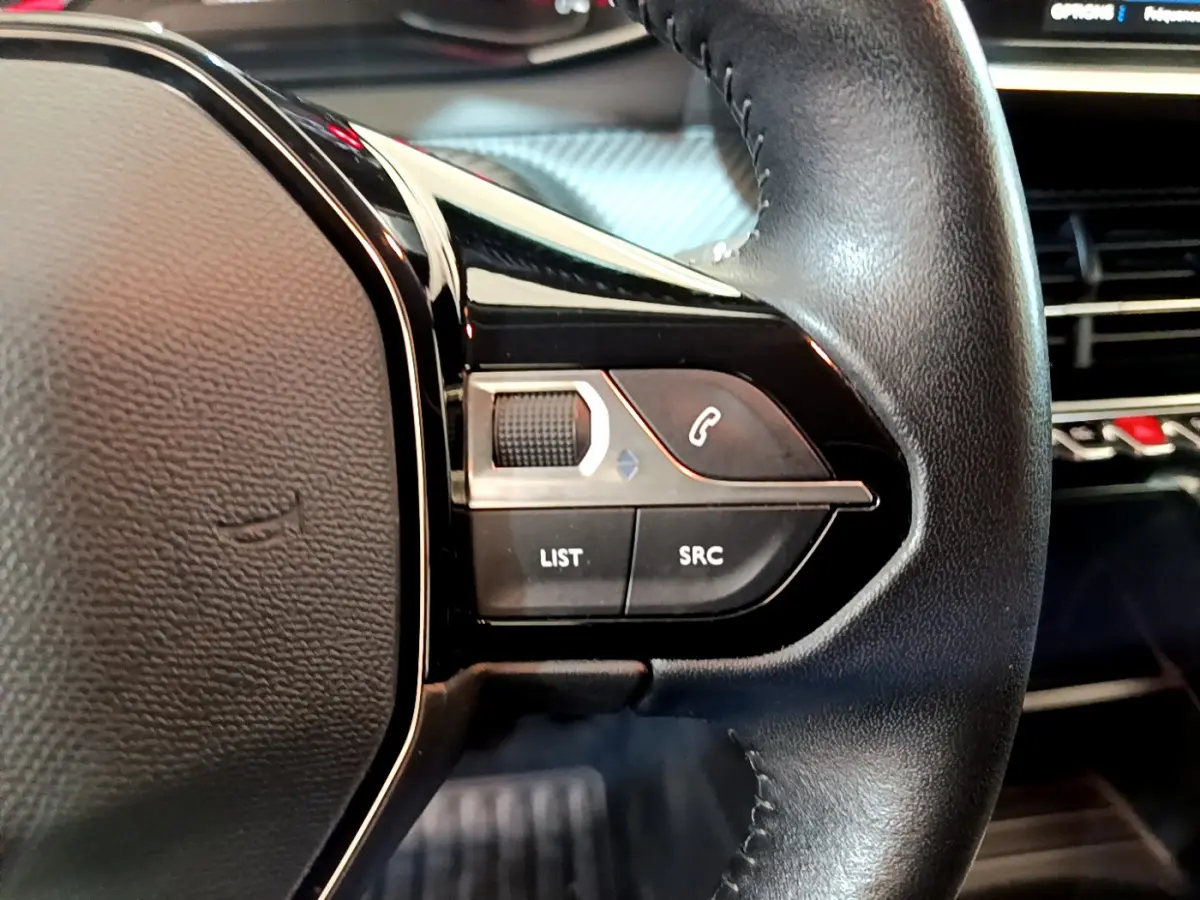 Gros plan sur les commandes gauche du volant cuir noir du Peugeot 2008 gris clair, avec tableau de bord en arrière-plan.