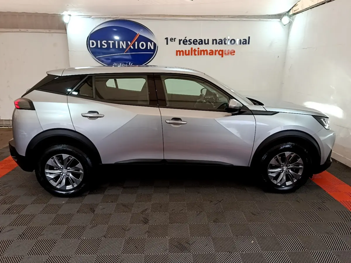 Peugeot 2008 gris clair vue de profil côté gauche, avec jantes alliage et toit noir contrasté en intérieur showroom.