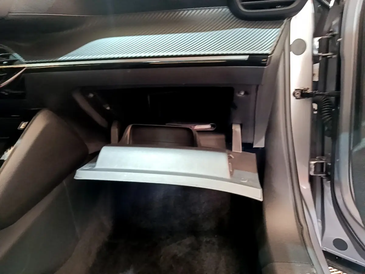 Gros plan sur la boîte à gants ouverte côté passager du Peugeot 2008 gris clair, montrant l'intérieur noir et le tableau de bord.