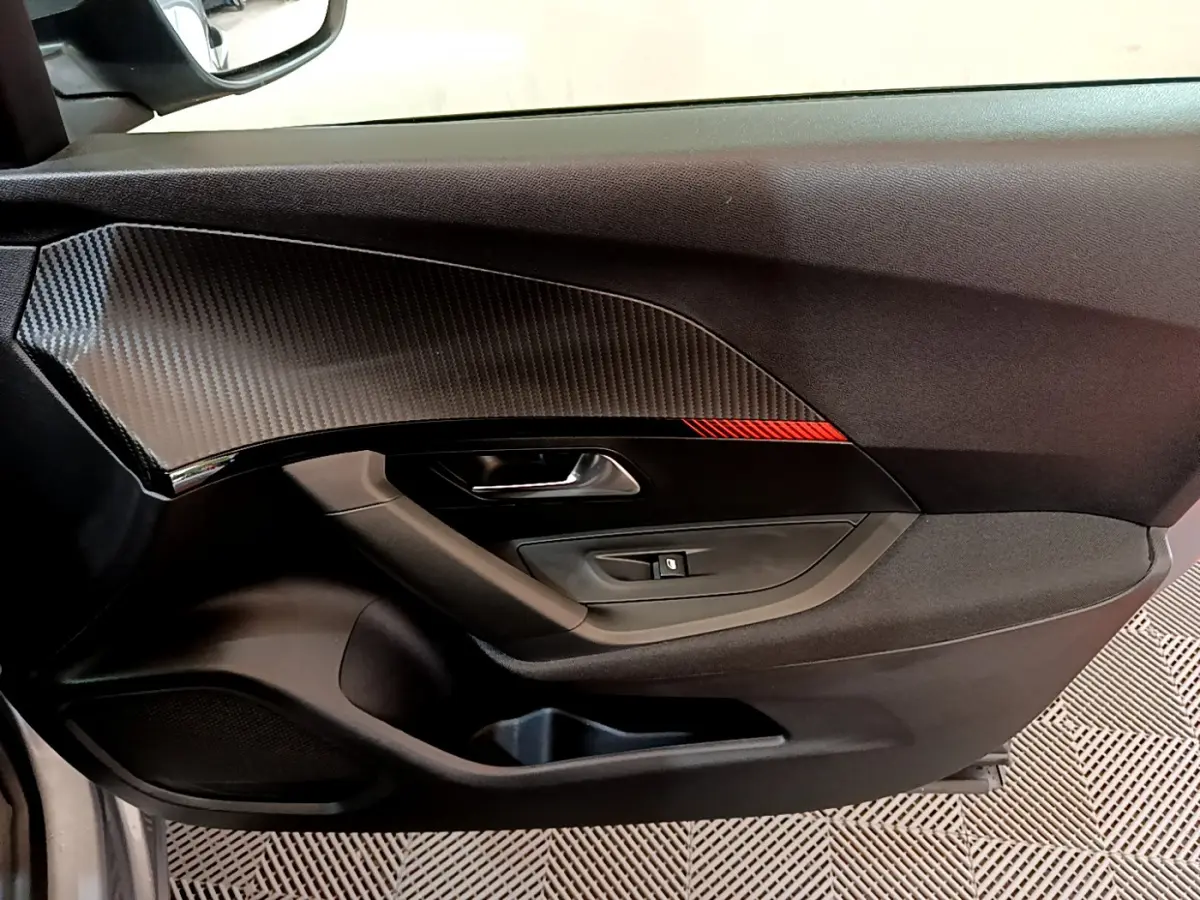 Détail de la porte côté conducteur avec insert imitation carbone et bande rouge sur Peugeot 2008 gris clair 2020.
