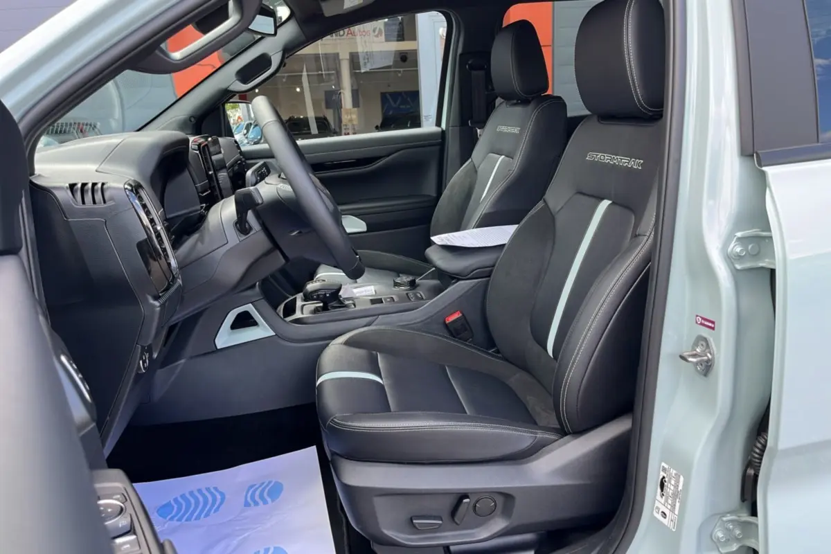 Vue intérieure côté conducteur du Ford Ranger gris zen 2026, sièges noirs Stormtrak avec surpiqûres blanches et volant multifonctions.