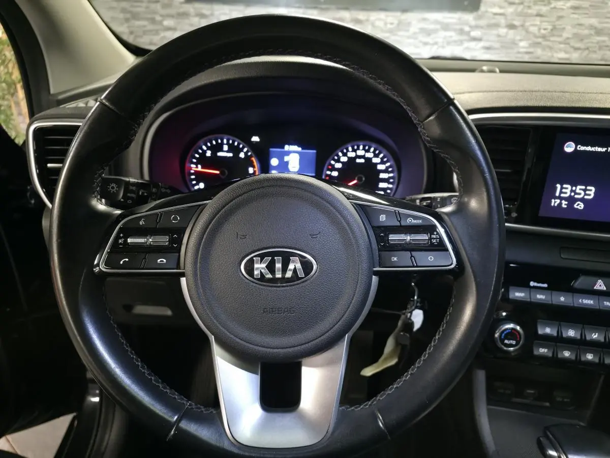 Vue rapprochée du volant cuir noir KIA avec commandes intégrées et tableau de bord éclairé du Sportage 2021.