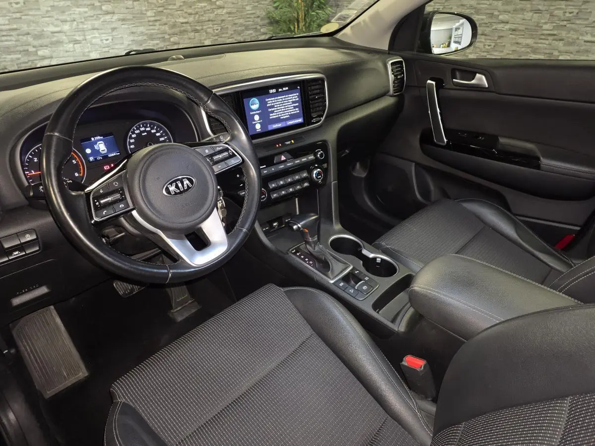 Vue intérieure côté conducteur du Kia Sportage 1.6 CRDI MHEV noir, montrant tableau de bord et console centrale avec volant cuir.