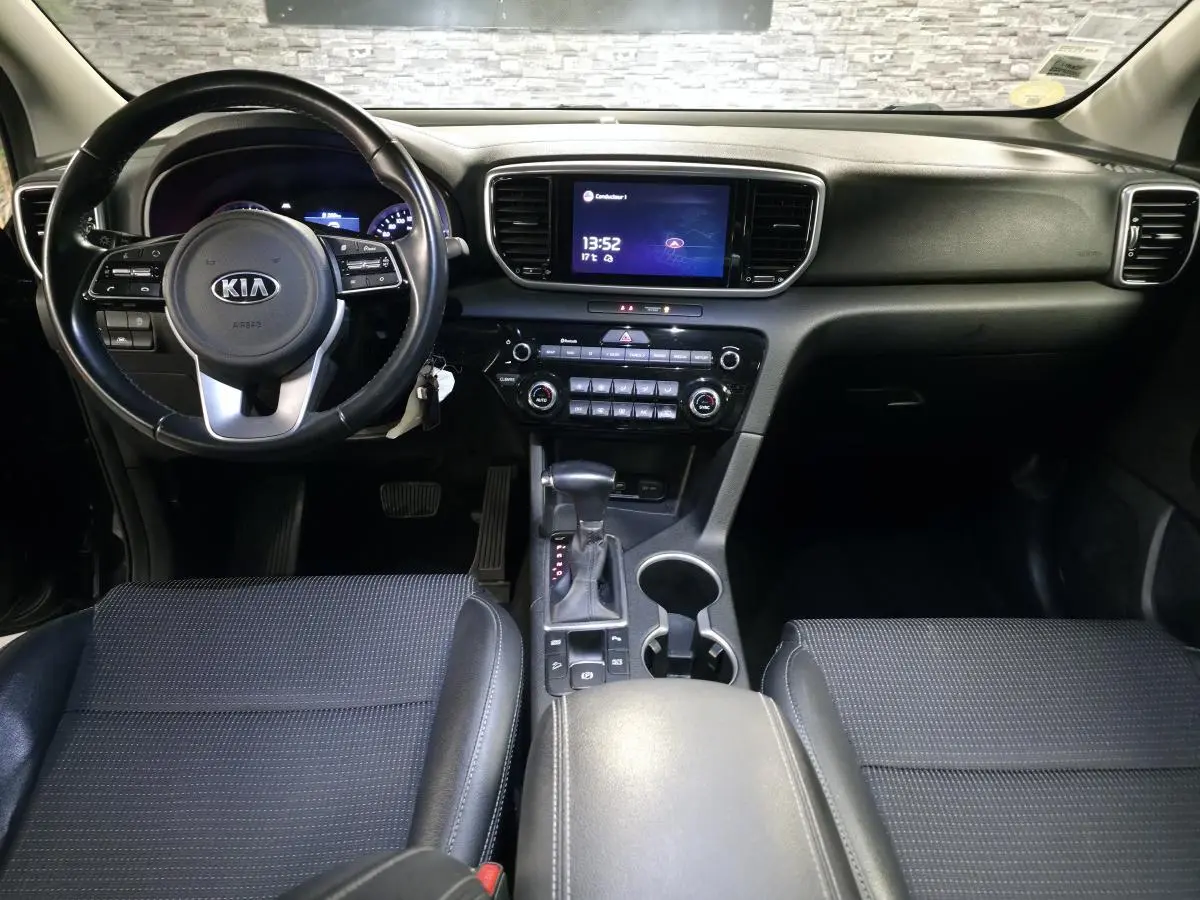 Vue intérieure avant du Kia Sportage noir, tableau de bord avec écran tactile 8 pouces et volant cuir multifonction.