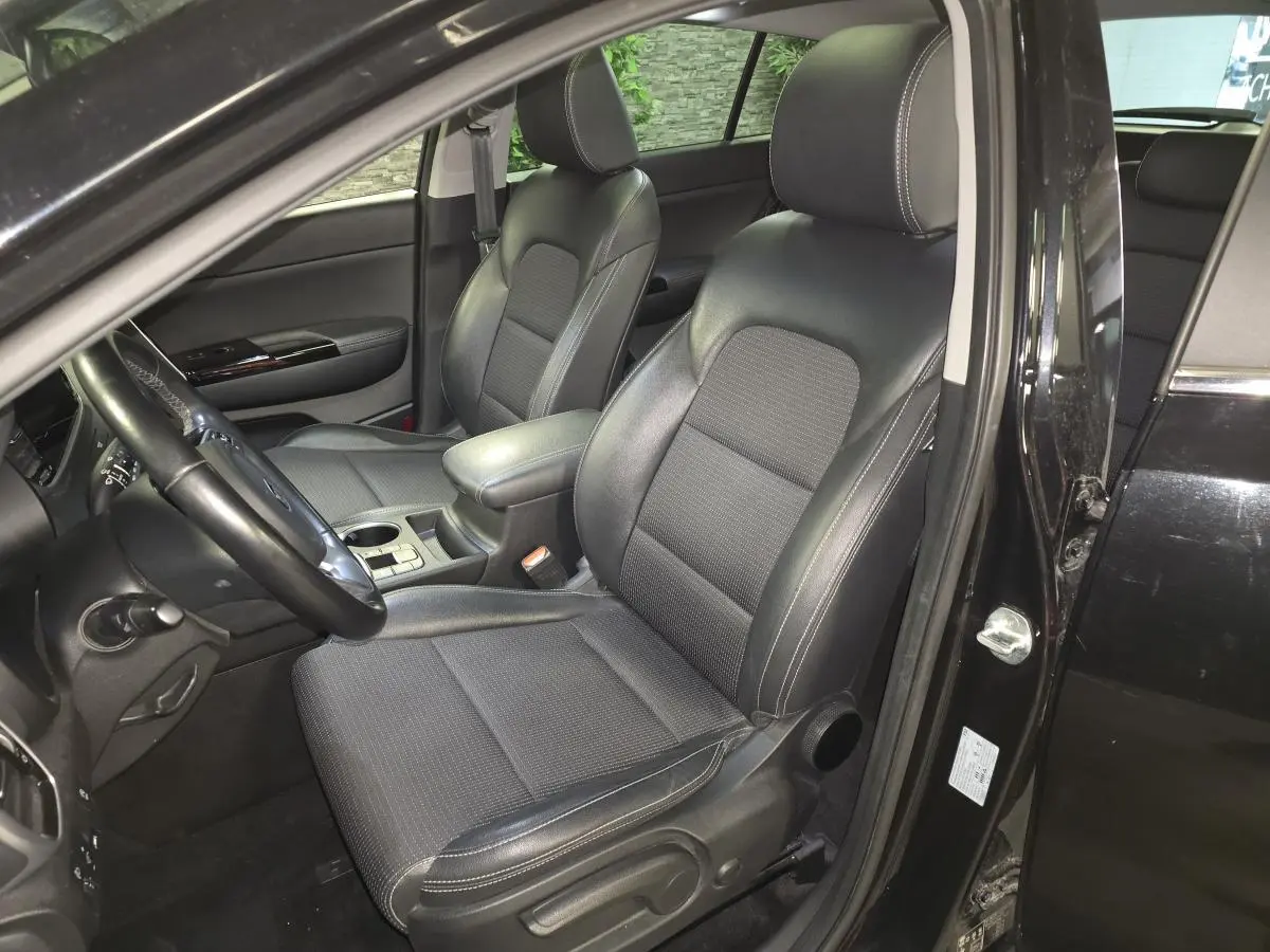 Vue intérieure côté conducteur du Kia Sportage noir 2021, mettant en valeur les sièges cuir/tissu et l'accoudoir central.