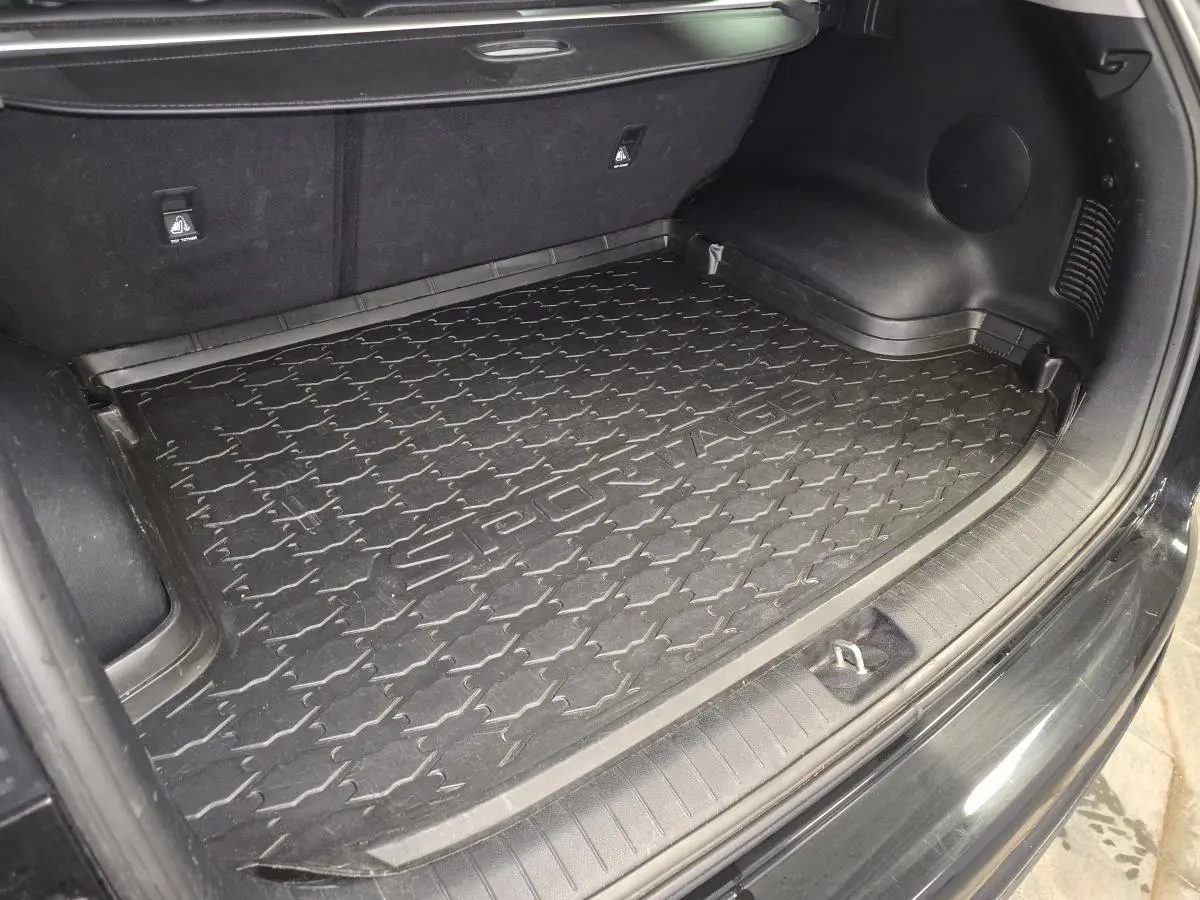 Coffre ouvert vu de l'arrière d'un KIA Sportage noir avec tapis de coffre caoutchouc marqué Sportage.