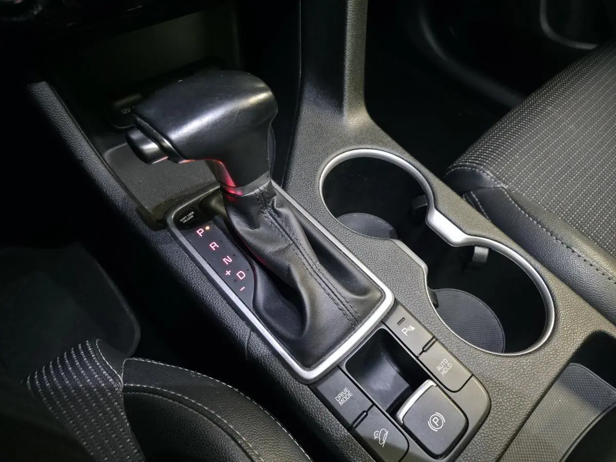Gros plan sur la console centrale du Kia Sportage noir, mettant en valeur le levier de vitesses automatique et les porte-gobelets.