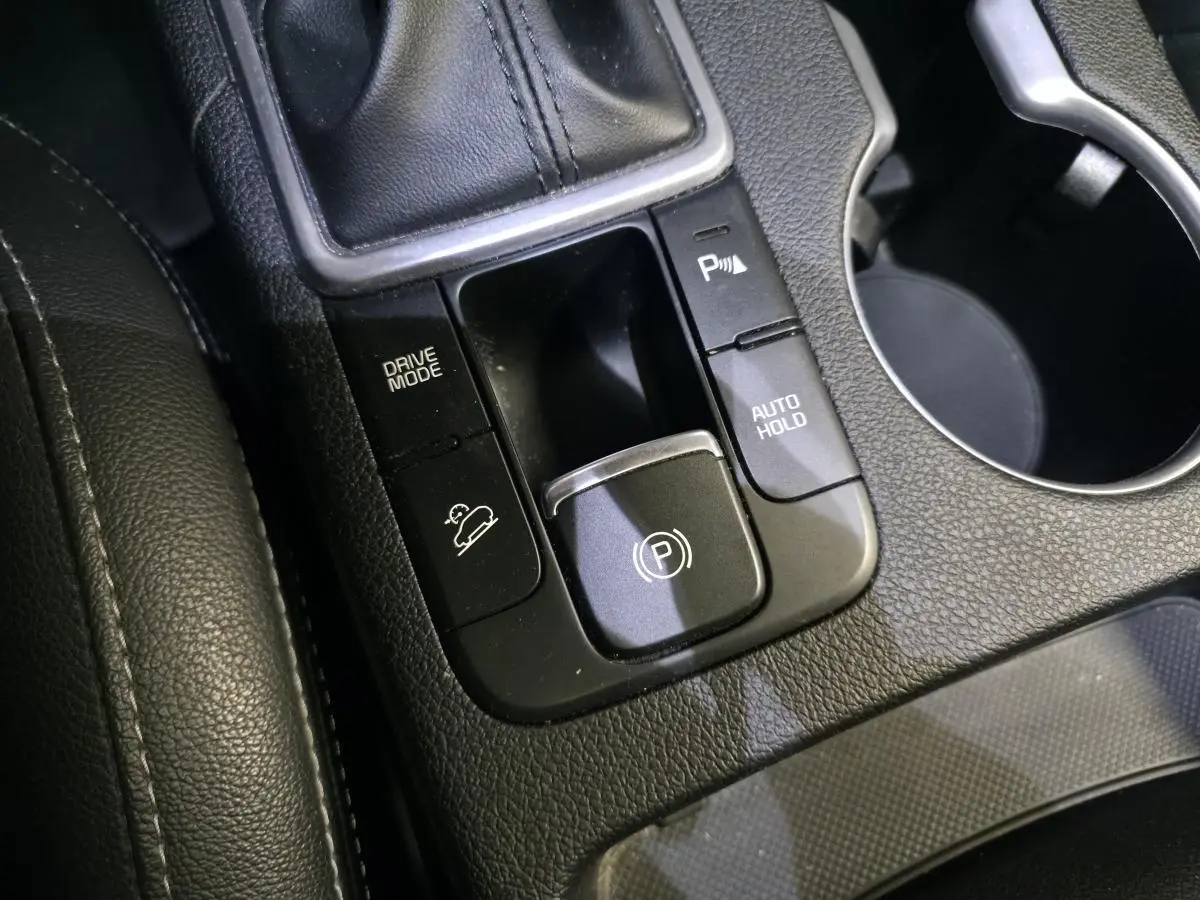 Gros plan sur la console centrale noire du Kia Sportage 2021 avec commandes frein électrique et mode de conduite.