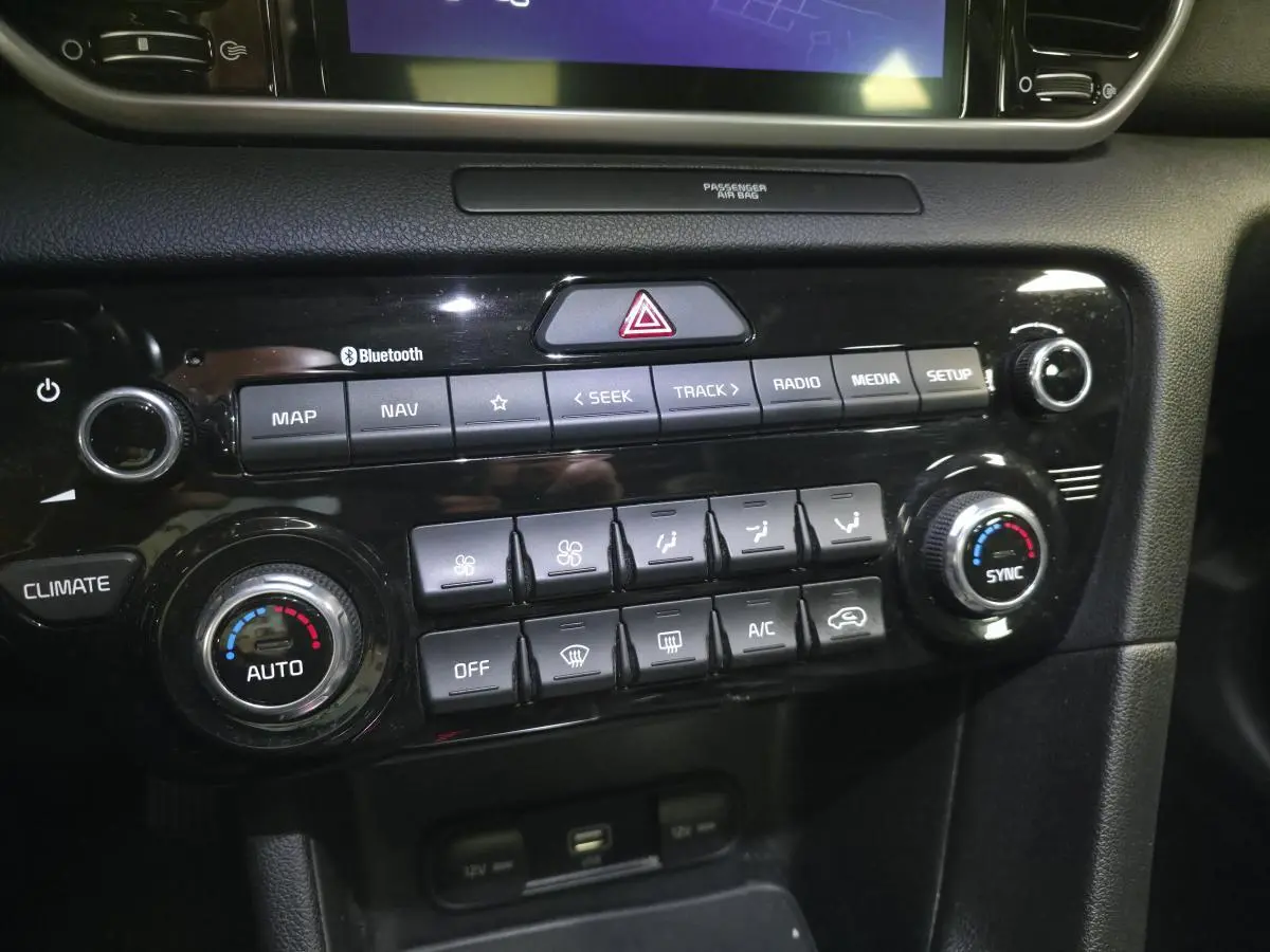 Gros plan sur la console centrale noire du Kia Sportage 1.6 CRDI MHEV avec commandes climatisation et multimédia.