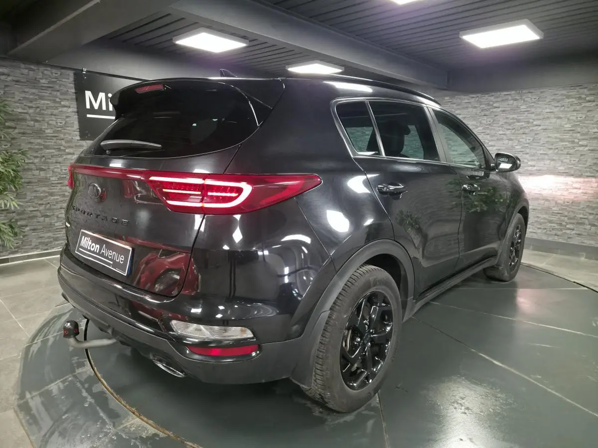 Vue 3/4 arrière droite du KIA Sportage noir Black Edition 2021 avec jantes noires et feux arrière LED allumés.
