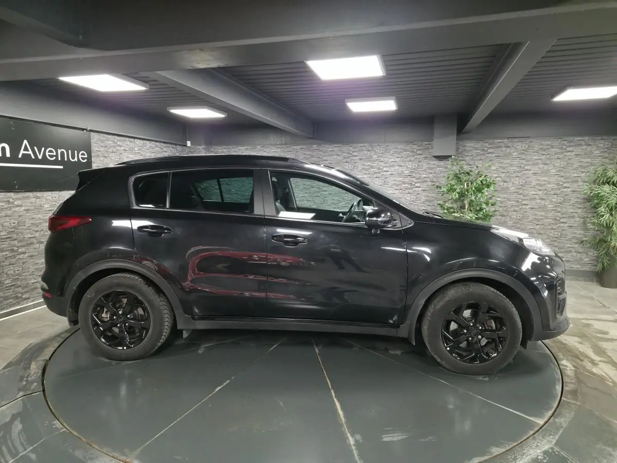 Vue de profil côté gauche d’un KIA Sportage noir 2021 avec jantes alliage noires Black Edition dans un showroom.