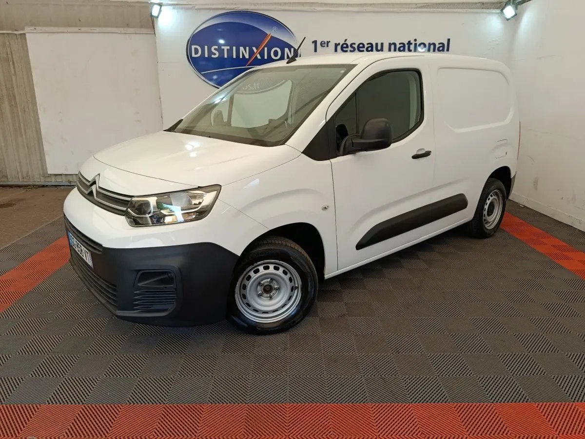 Vue 3/4 avant droit d'un Citroën Berlingo blanc 2022 avec pare-chocs noir et jantes acier en intérieur showroom.