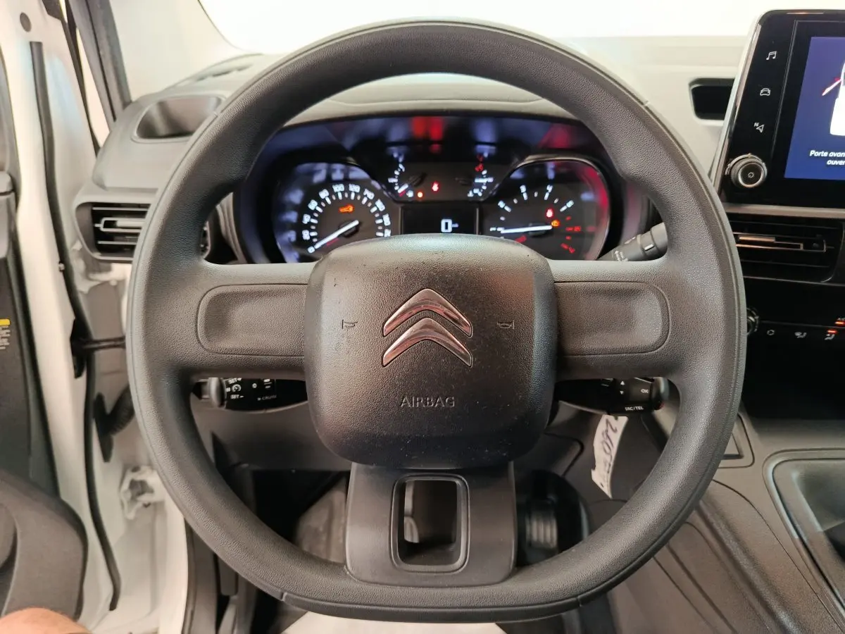 Vue centrée sur le volant noir du Citroën Berlingo blanc, avec tableau de bord et écran tactile visibles à droite.