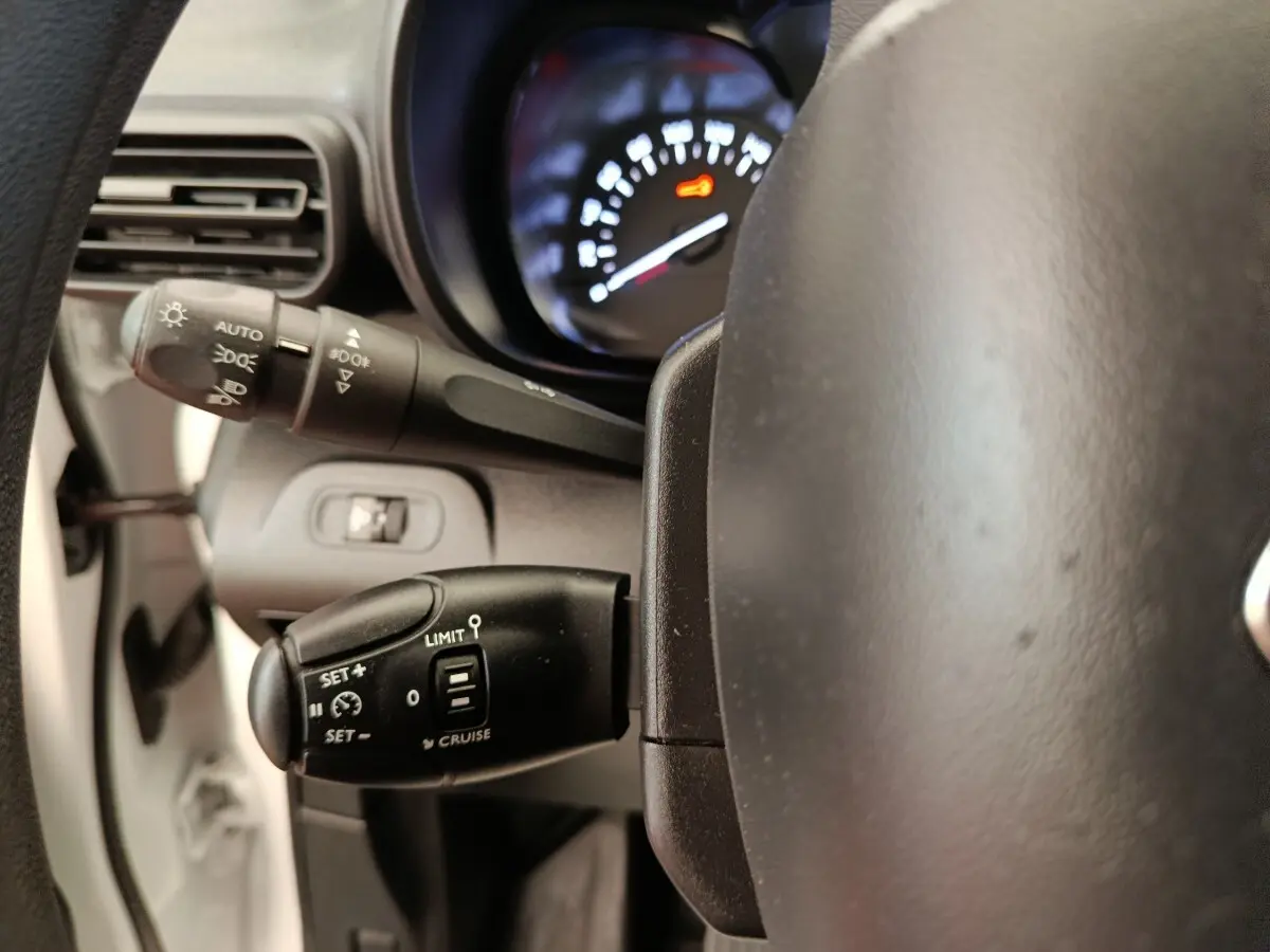 Gros plan sur le volant et commandes au volant du Citroën Berlingo blanc, affichage du compteur partiellement visible.