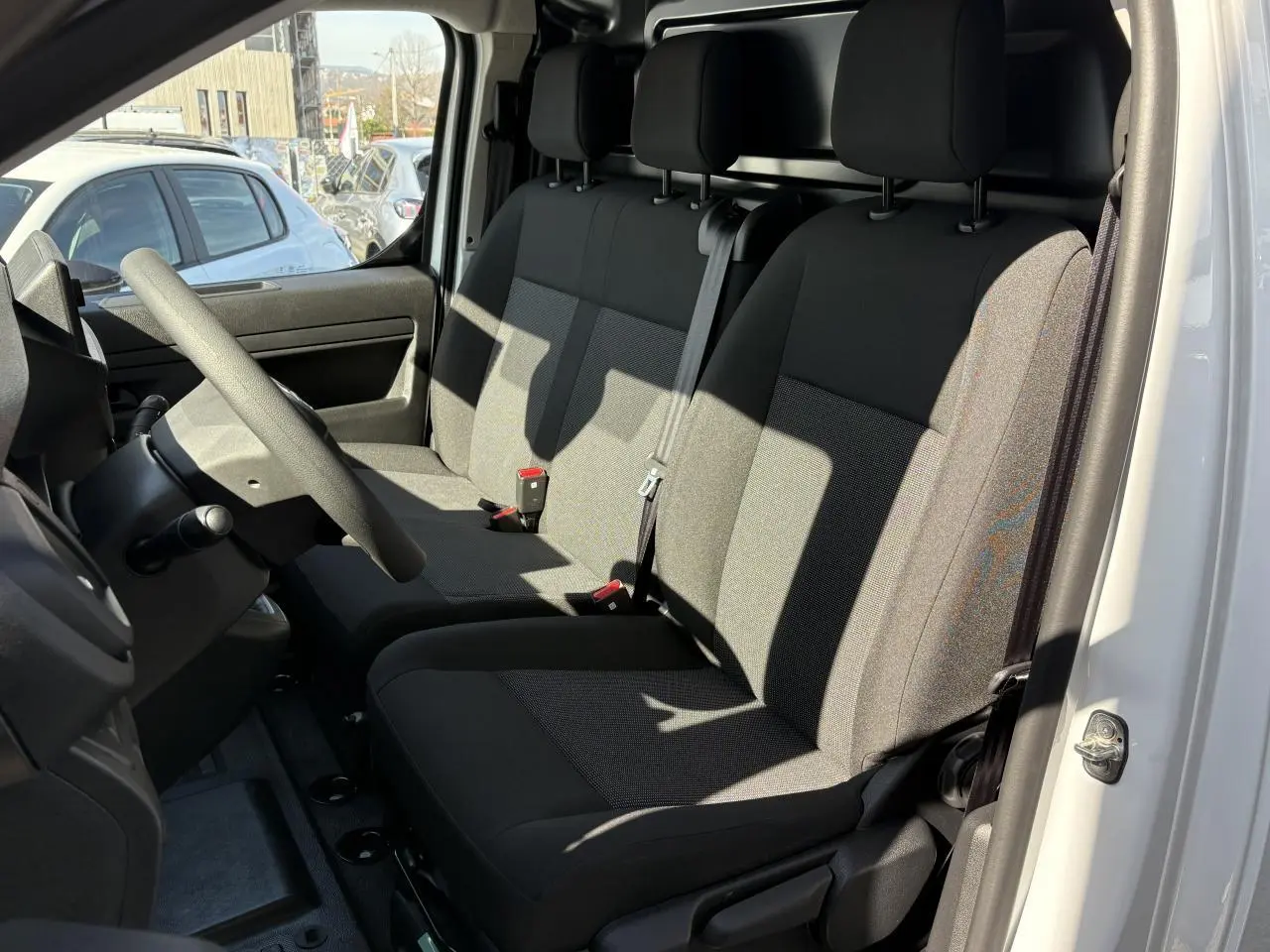 Vue intérieure côté conducteur de l'Opel Vivaro blanc 2024, montrant la banquette tissu bi-ton noir/gris et le volant réglable.