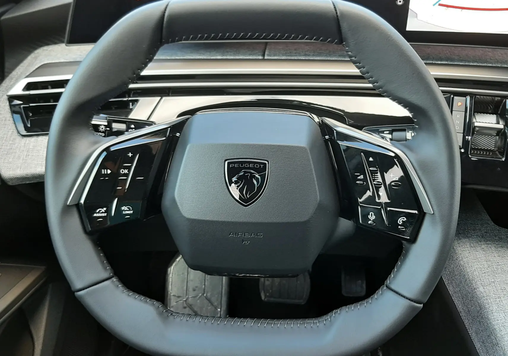 Gros plan sur le volant carré du Peugeot 5008 2025, avec commandes tactiles et tableau de bord numérique visible.