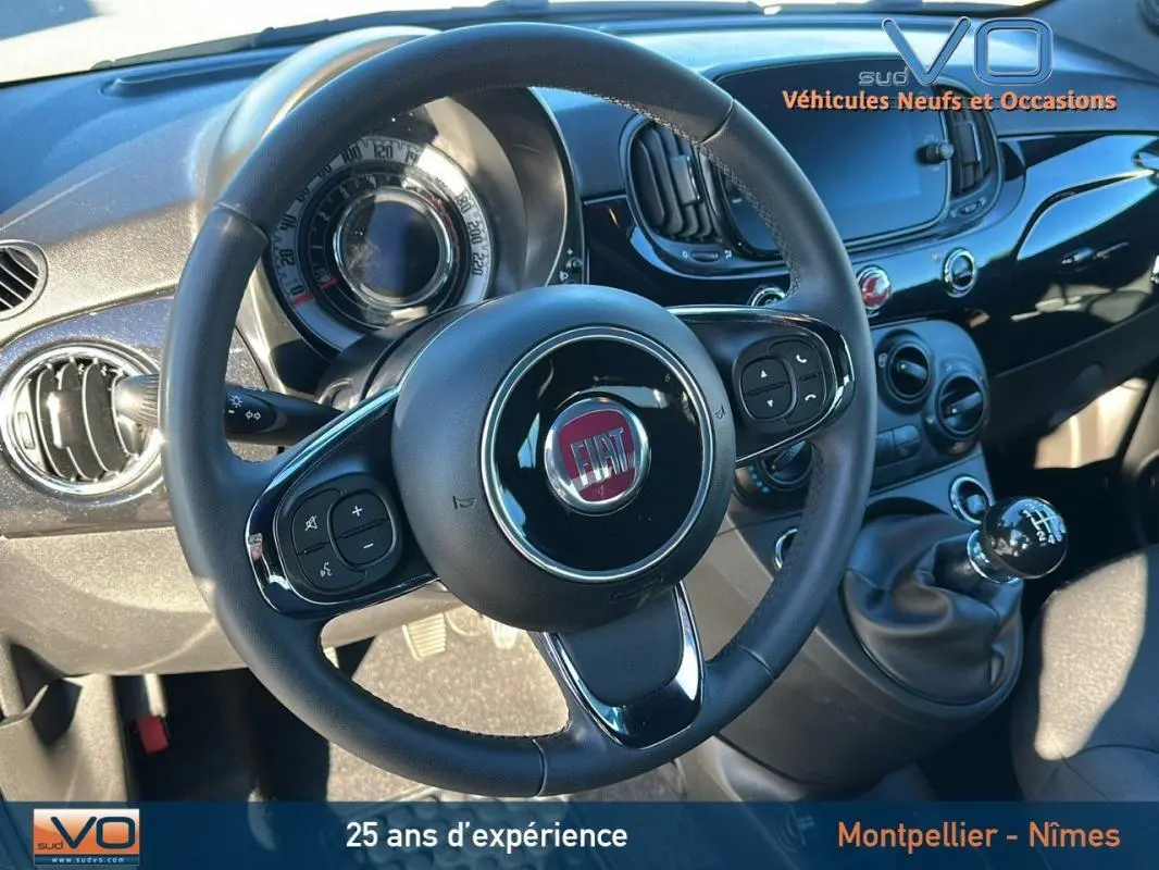 Vue rapprochée de l'intérieur du Fiat 500C 2024 noir, mettant en valeur le volant, le tableau de bord et la boîte manuelle.