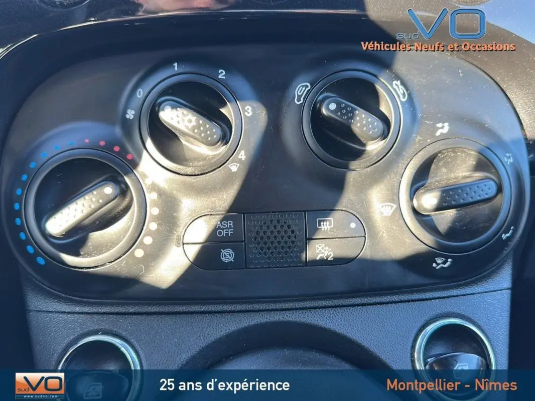 Gros plan sur les commandes de climatisation de la FIAT 500C noire 2024, version hybride avec options visibles.