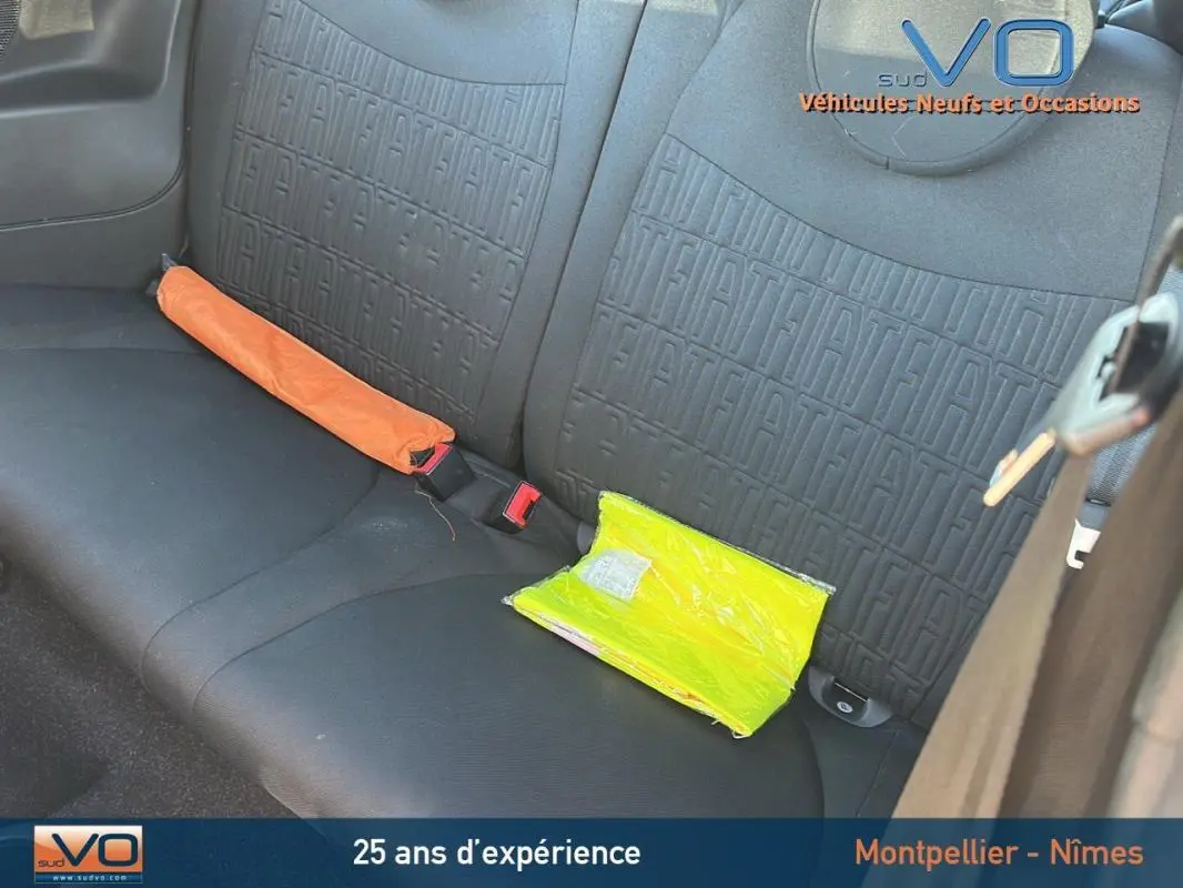 Vue intérieure sur la banquette arrière noire embossée du logo FIAT avec un gilet jaune et un triangle de signalisation.