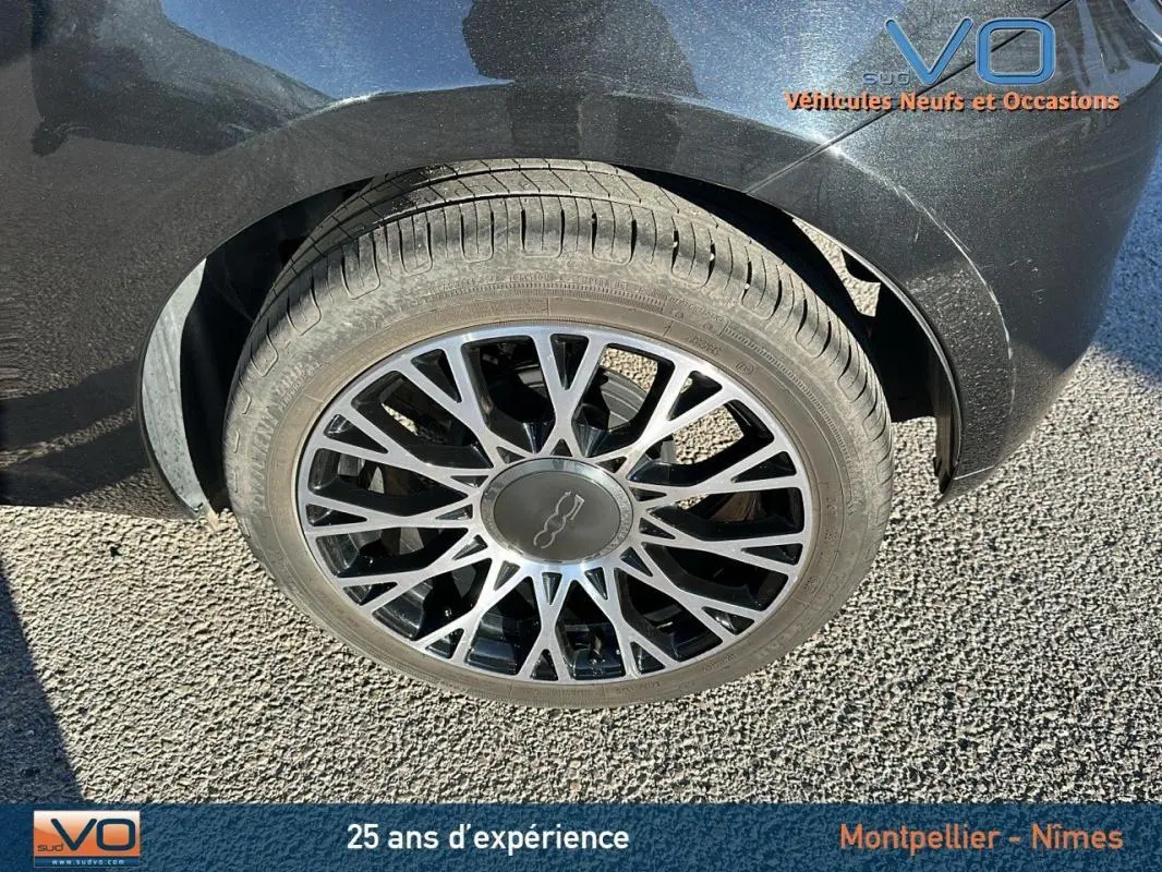 Gros plan sur la roue avant gauche d'une FIAT 500C noire 2024, mettant en valeur la jante au design complexe.