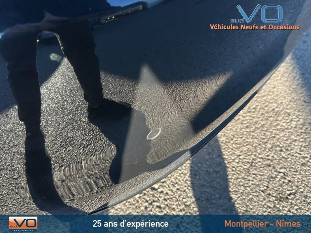 Reflet d'une personne debout sur le capot noir brillant d'une Fiat 500C 2024 hybride, vue rapprochée extérieure.