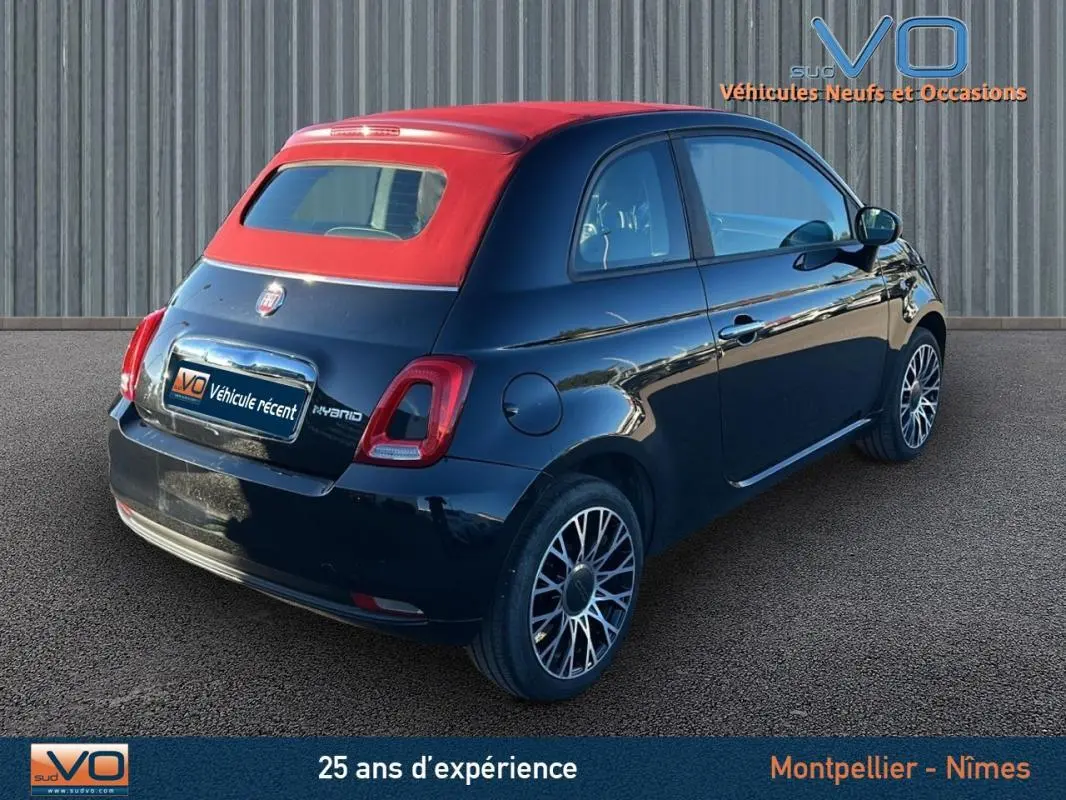 Vue 3/4 arrière droite d'une FIAT 500C noire 2024 avec toit rouge et jantes stylisées, version hybride essence.