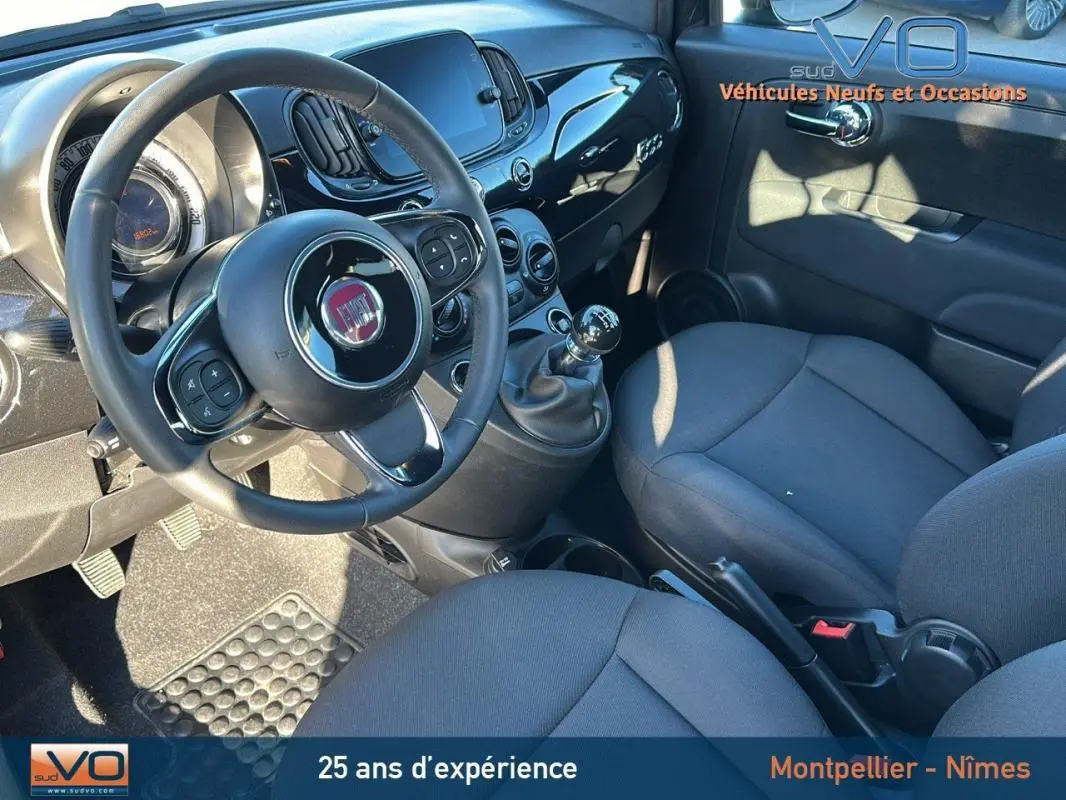 Intérieur du Fiat 500C 2024 noir, vue côté conducteur montrant le volant, tableau de bord et levier de vitesse manuel.
