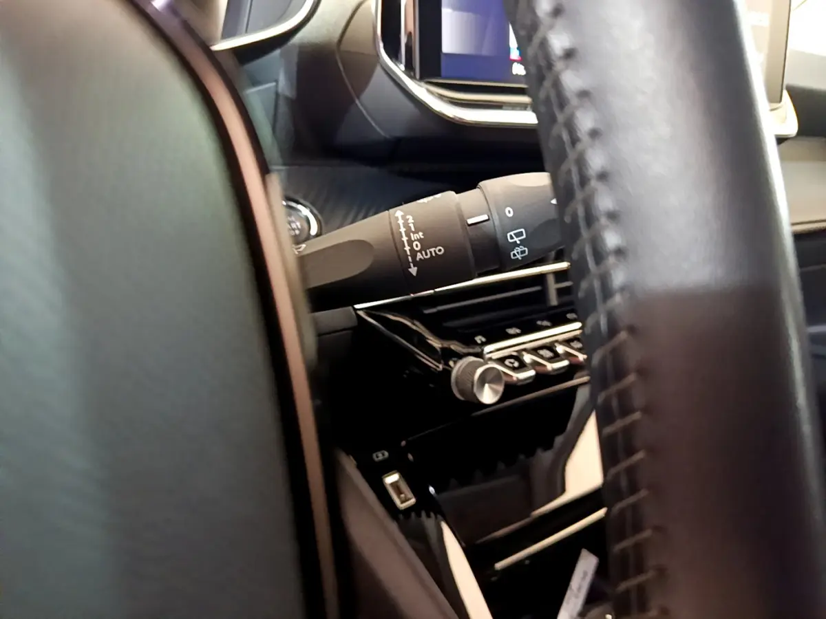 Détail du commodo d’essuie-glace côté gauche et partie du volant cuir dans l’habitacle noir du Peugeot 2008.