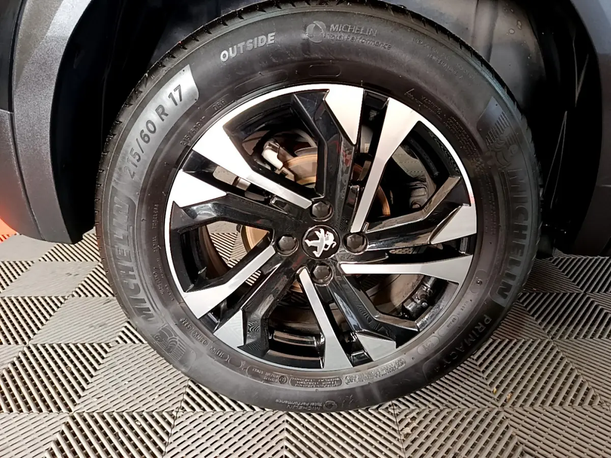 Gros plan sur la jante alliage noire et argentée avec logo Peugeot d’un PEUGEOT 2008 noir.