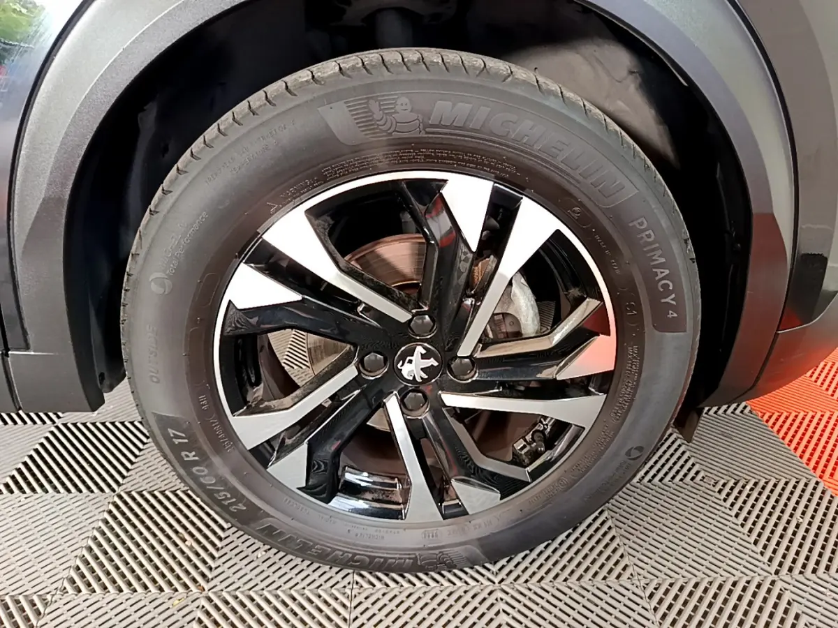 Gros plan sur la roue avant gauche du Peugeot 2008 noir, mettant en valeur la jante alliage bicolore et le pneu Michelin.