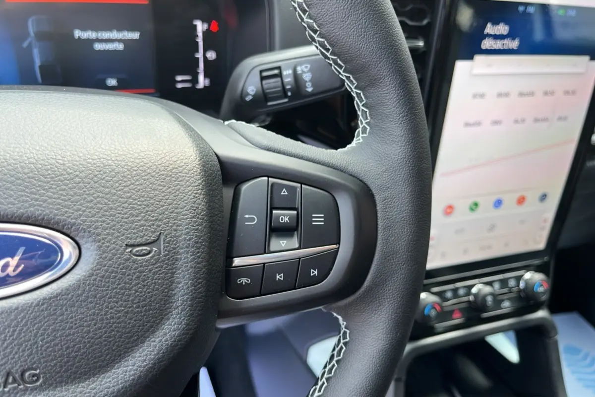 Gros plan sur le volant cuir noir avec commandes multifonctions du Ford Ranger gris zen, écran tactile et tableau de bord en arrière-plan.