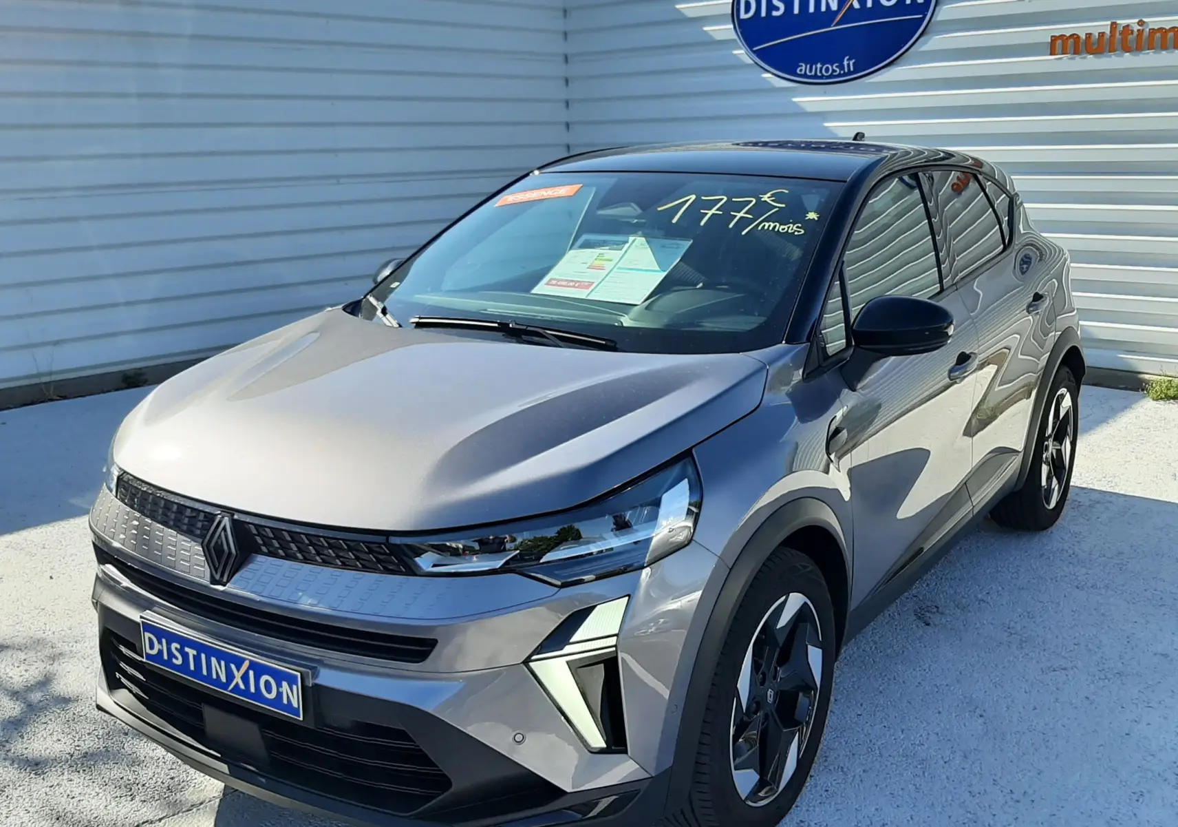 Renault Captur II gris Cassiopée en 3/4 avant droit, avec jantes bi-ton et calandre moderne sous un ciel ensoleillé.