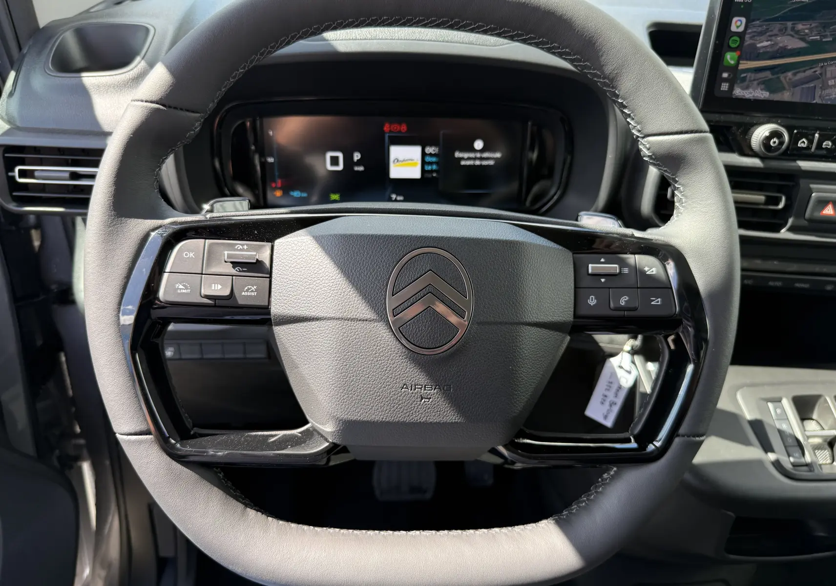 Vue frontale du volant en cuir noir du Citroën Berlingo gris Artense, avec commandes intégrées et tableau de bord numérique.