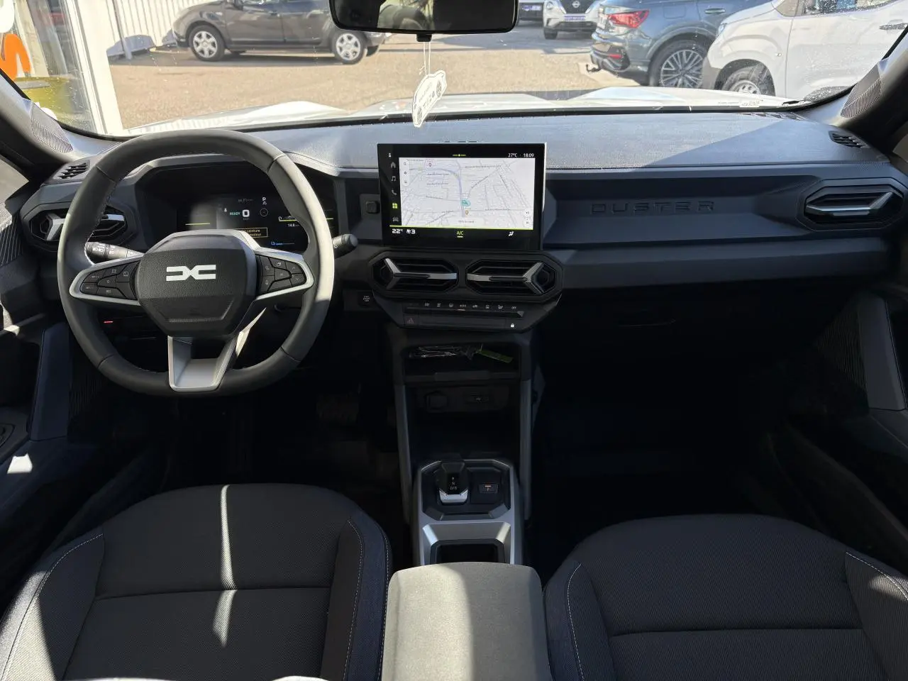 Vue intérieure avant du Dacia Duster 2024, tableau de bord noir avec écran tactile central et volant multifonction.