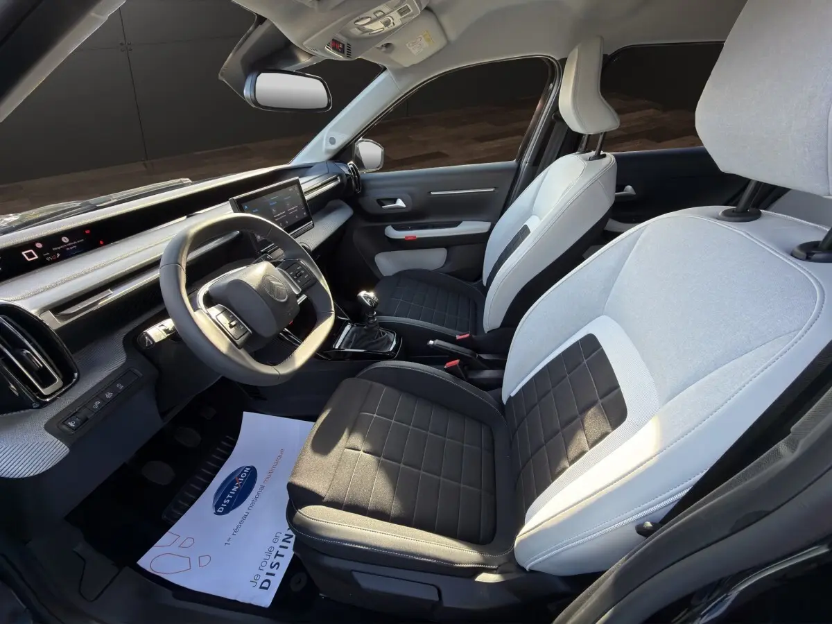Vue intérieure côté conducteur de la Citroën C3 2025, sièges bicolores gris et noir, tableau de bord avec écran tactile.