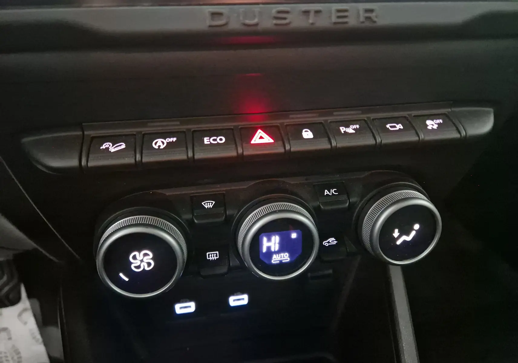 Gros plan sur la console centrale du Dacia Duster 2024, montrant les commandes de climatisation et les boutons de fonction éclairés.