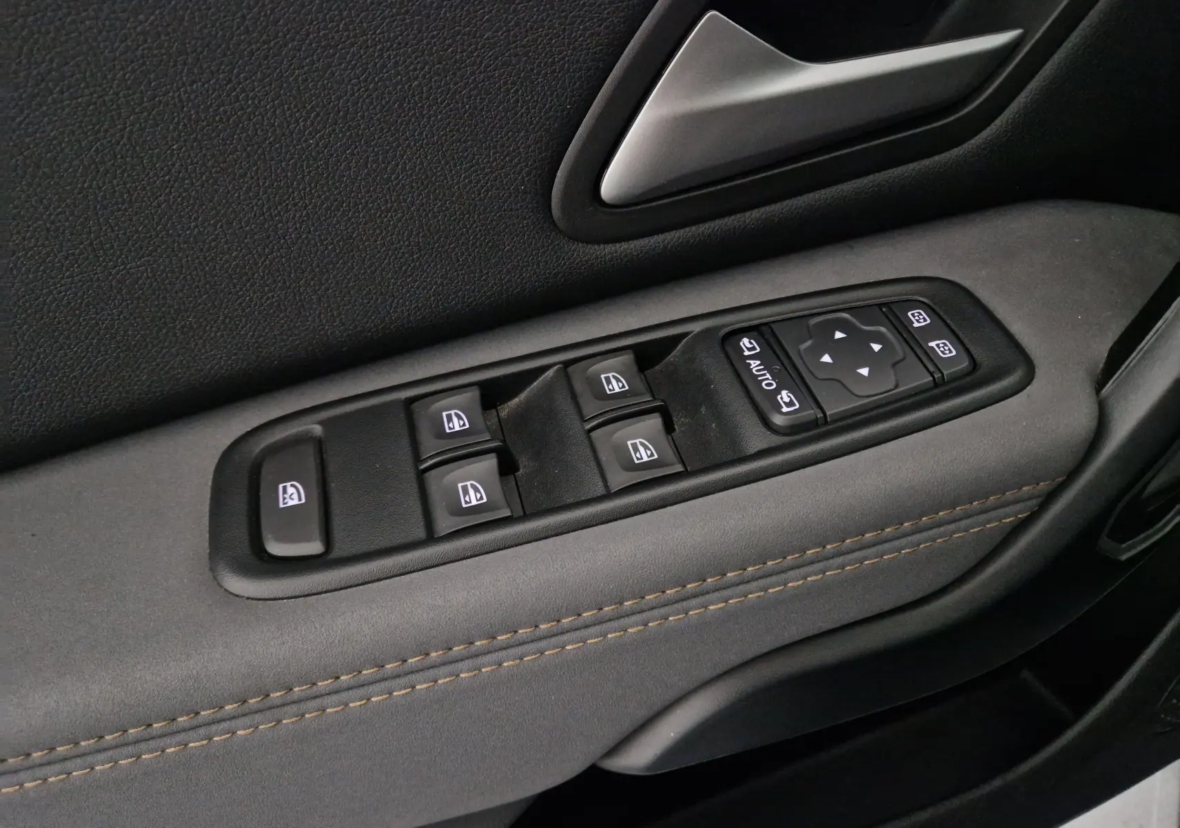 Gros plan sur les commandes de lève-vitres et rétroviseurs côté gauche du Dacia Duster blanc 2024.