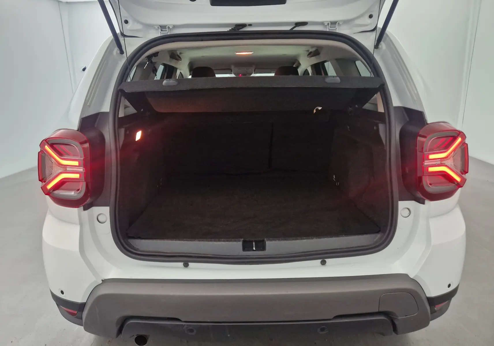 Vue arrière du Dacia Duster blanc 2024 avec coffre ouvert et feux arrière allumés en forme de Y.