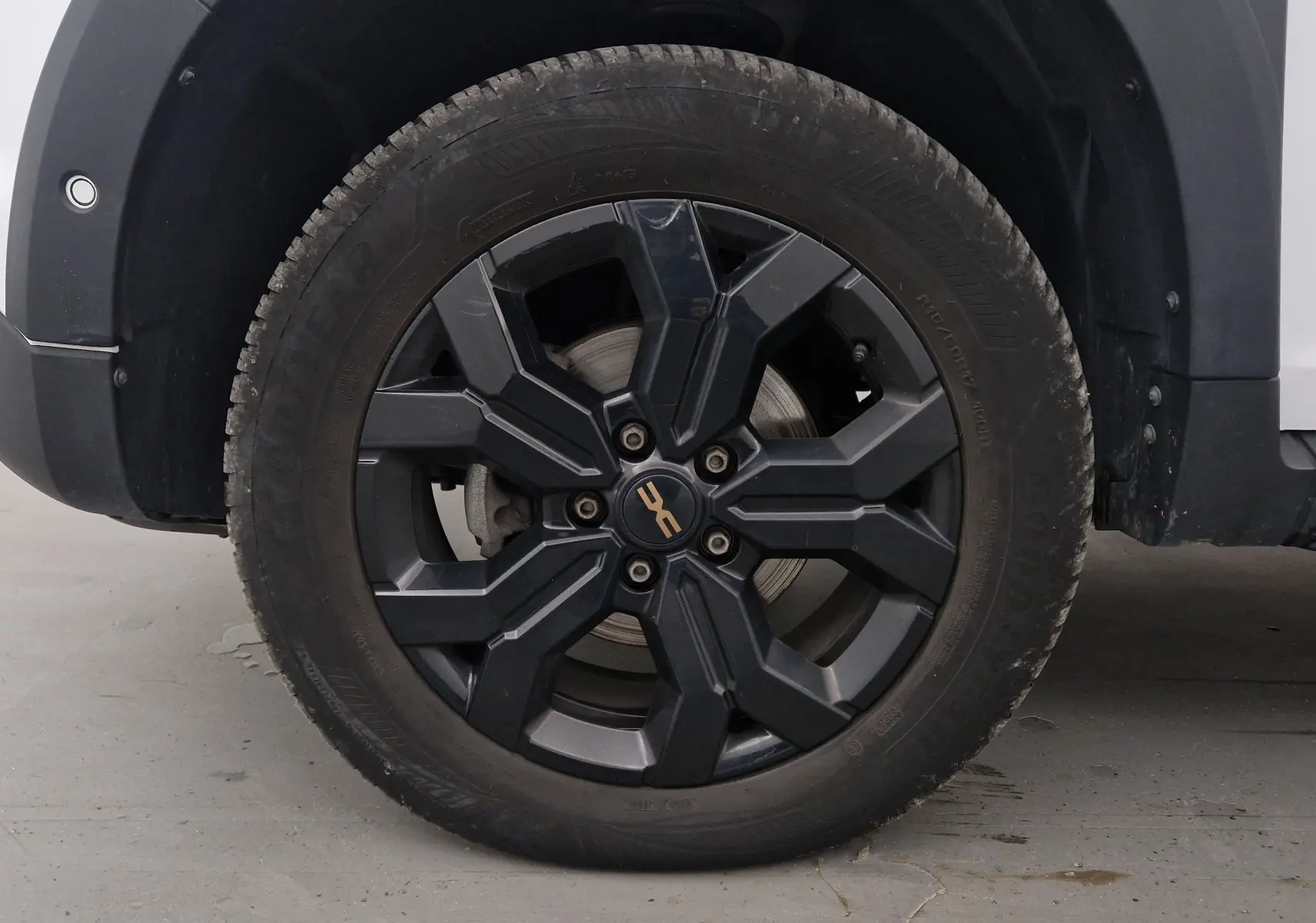 Gros plan sur la roue avant gauche du Dacia Duster blanc 2024, avec jante noire au design robuste et logo central doré.