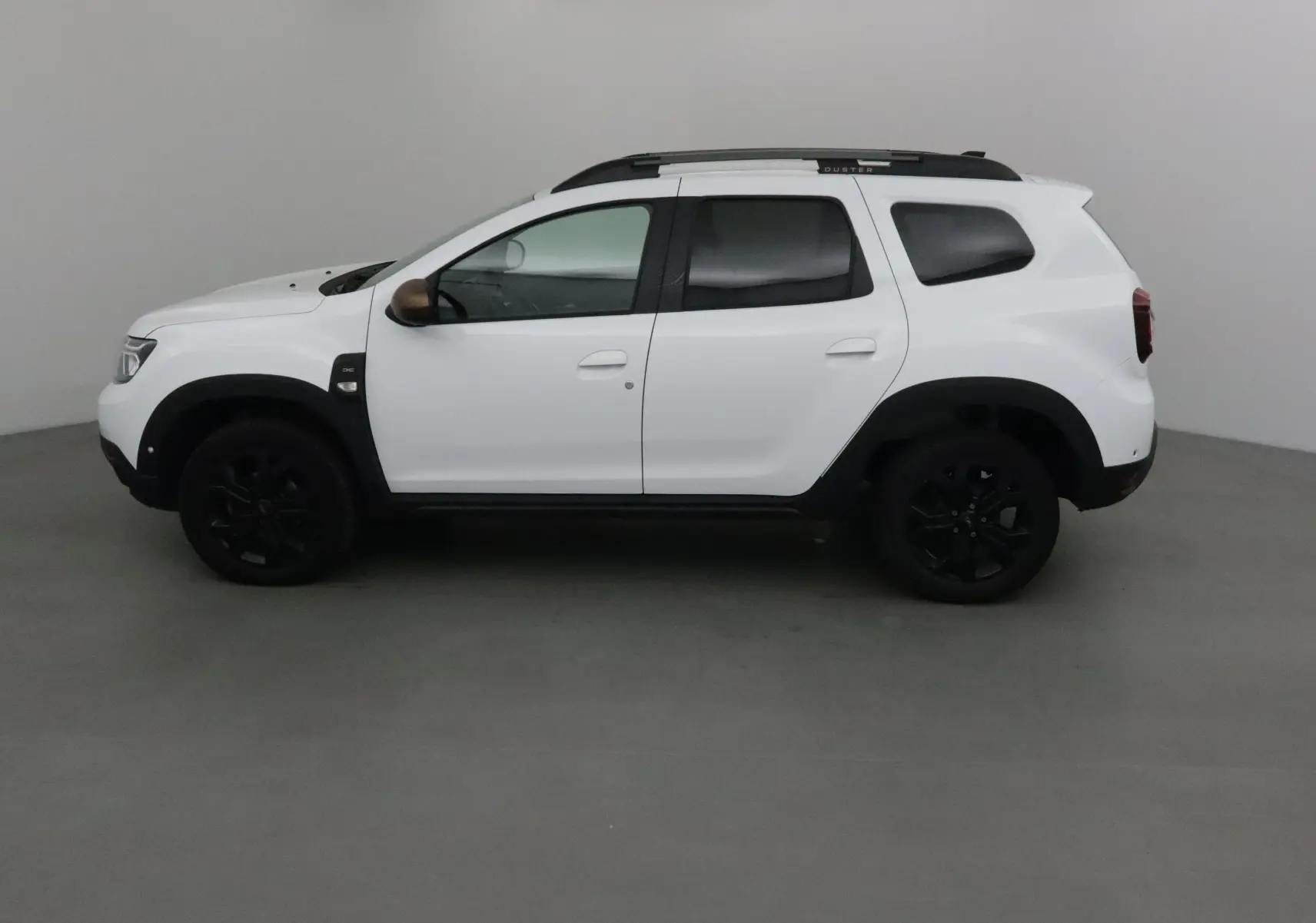 Profil côté gauche du Dacia Duster blanc 2024 avec jantes noires et barres de toit sombres, version 4x4 diesel.