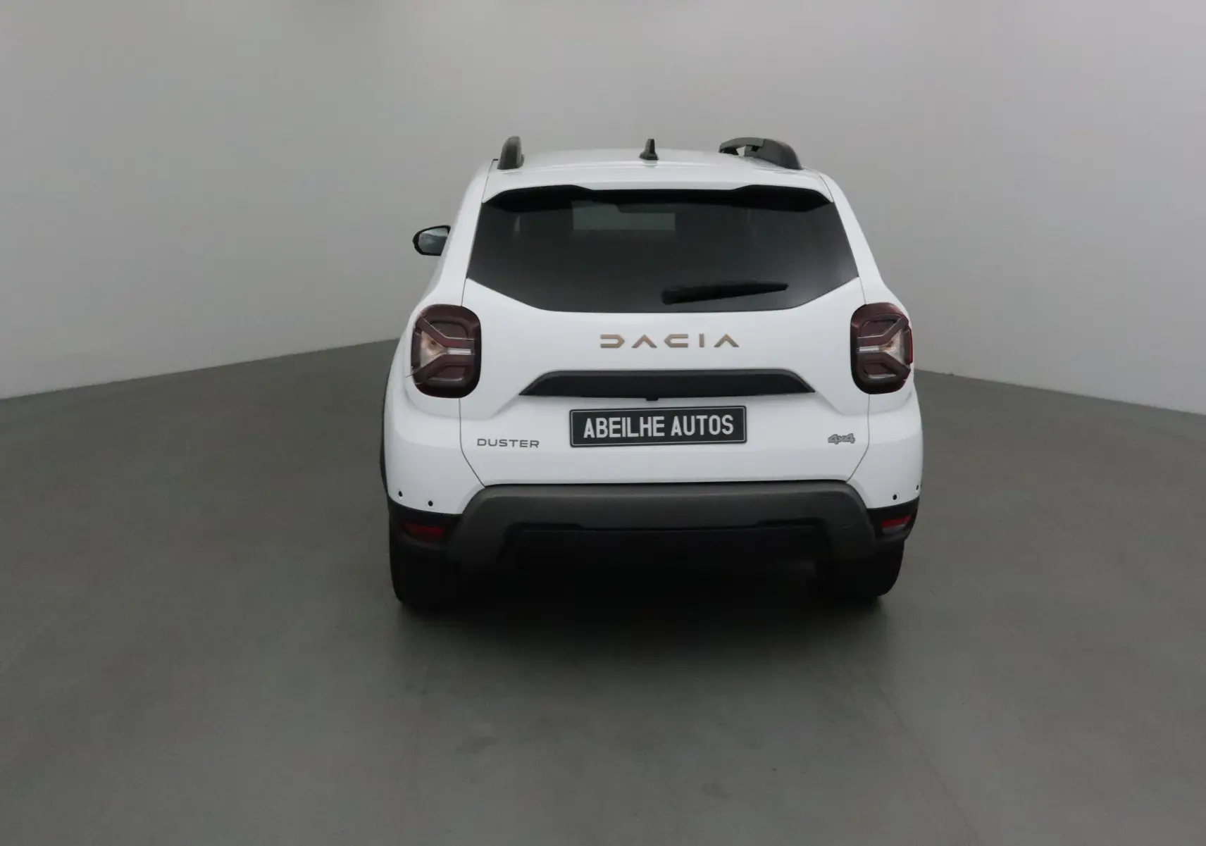 Vue arrière d'un Dacia Duster blanc 4x4 2024 avec logo et plaque Abeilhe Autos visible.