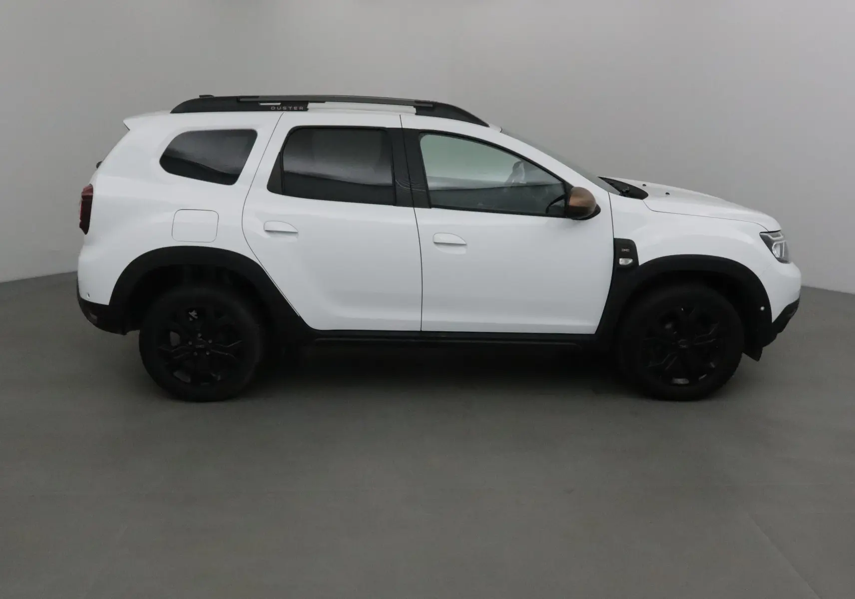 Profil côté gauche d'un Dacia Duster blanc 2024 avec jantes noires et coques de rétroviseurs marron.
