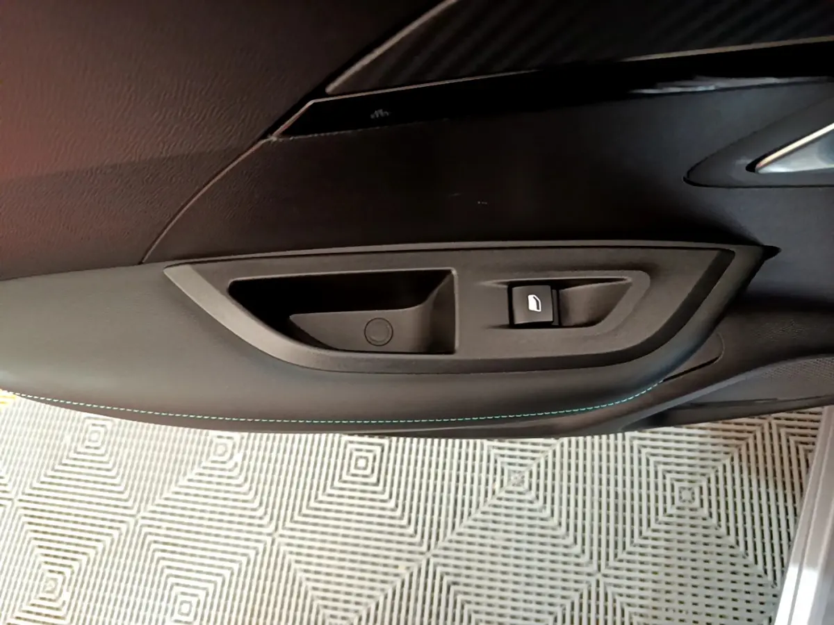 Poignée intérieure et commande de vitre côté gauche en plastique noir dans une Peugeot 2008 gris clair 2021.