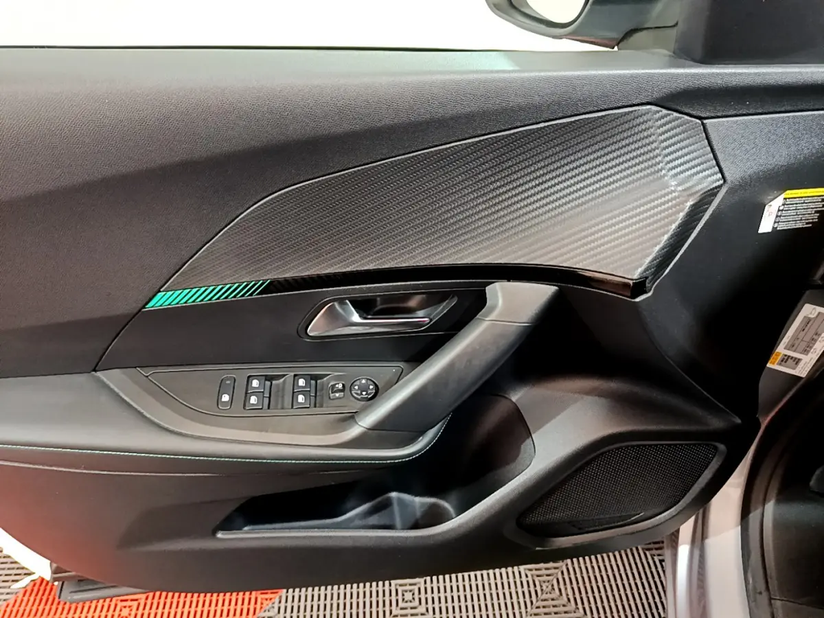 Vue rapprochée de la porte côté conducteur du Peugeot 2008 gris clair, avec insert imitation carbone et commandes électriques.
