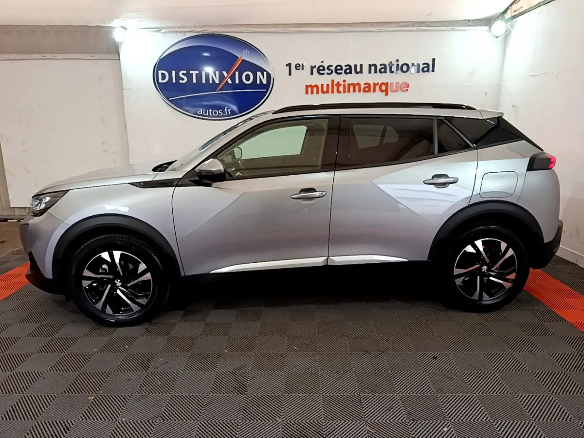 Profil côté gauche d'un Peugeot 2008 gris clair 2021 dans un showroom avec logo Distinxion en arrière-plan.