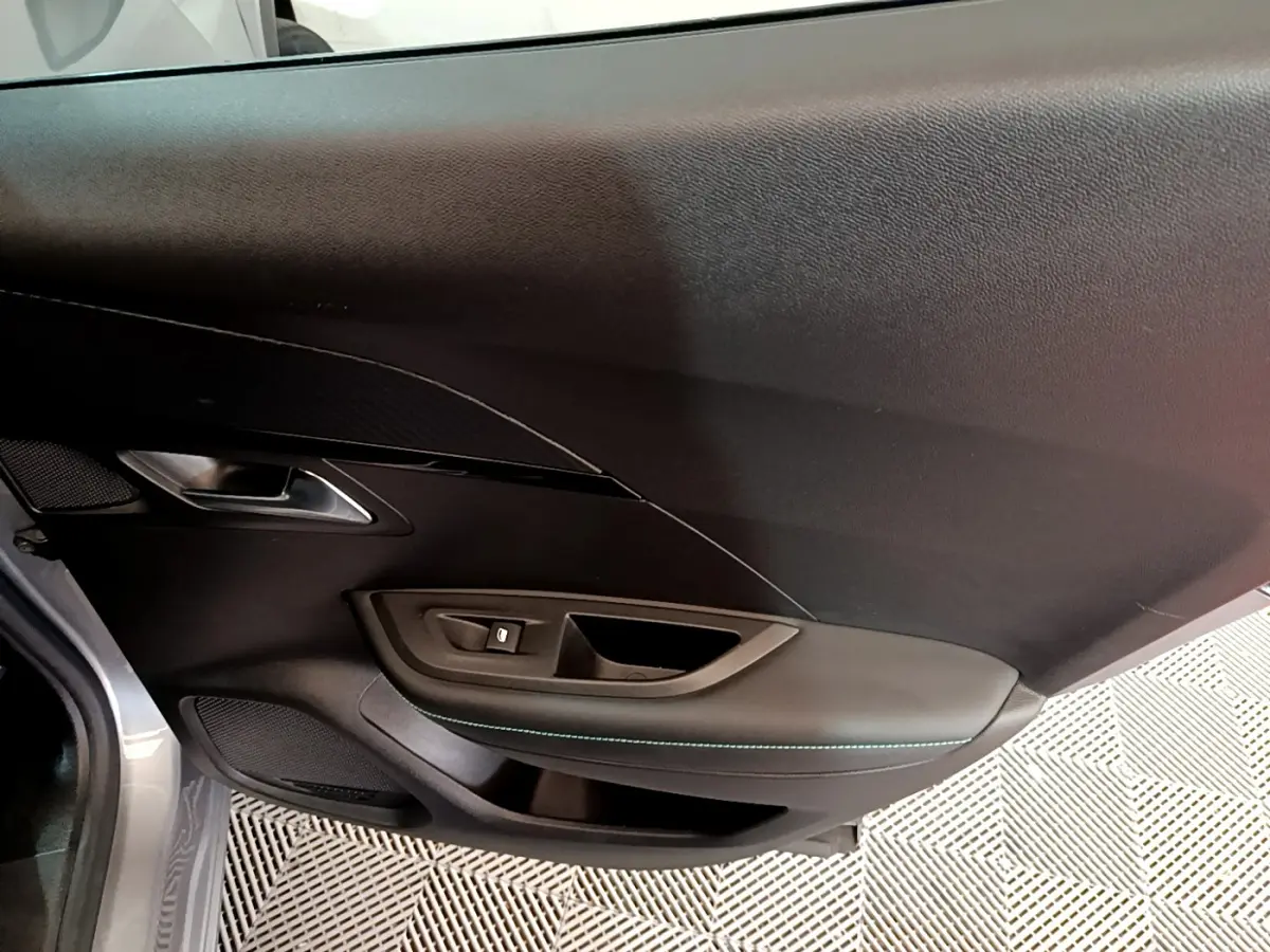 Gros plan sur la porte côté gauche du Peugeot 2008 gris clair, montrant la poignée et les commandes de vitre.