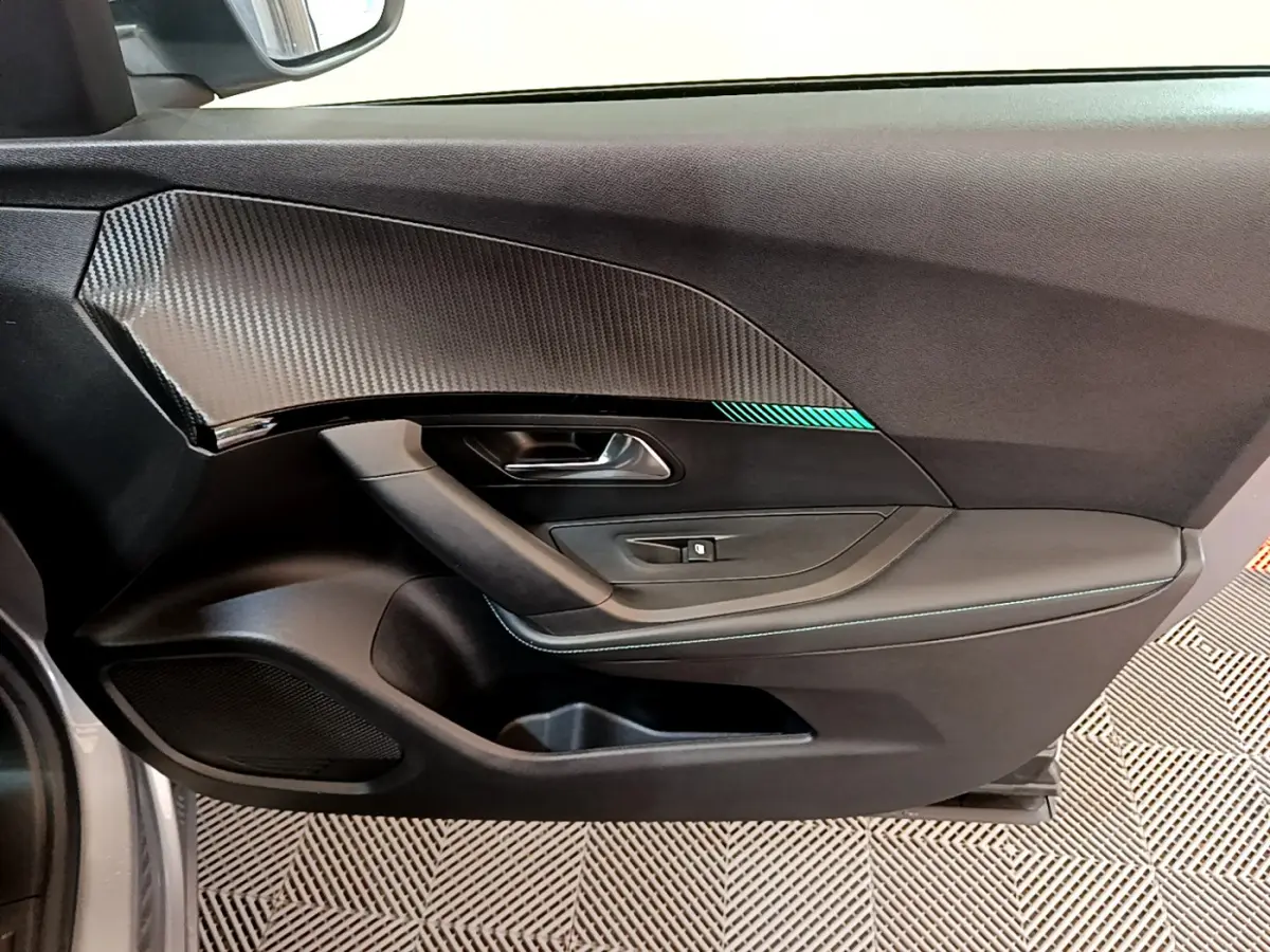 Vue intérieure côté gauche de la porte d'une Peugeot 2008 gris clair avec insert imitation carbone et surpiqûres bleues.